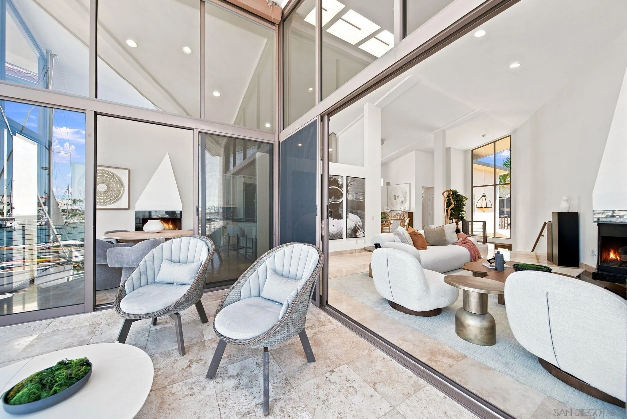 Staged living room with a tall ceiling, modern fireplace, and marina visible through floor-to-ceiling glass.