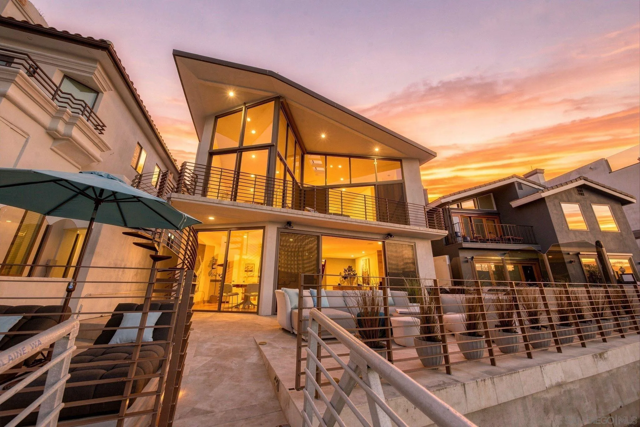 Modern glass-fronted home with furnished terraces glowing beneath an orange sunset.