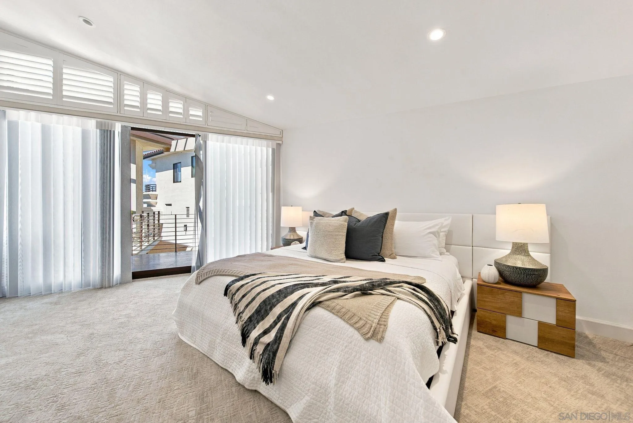 Staged bedroom with a white bed and a sliding glass door opening to a balcony.