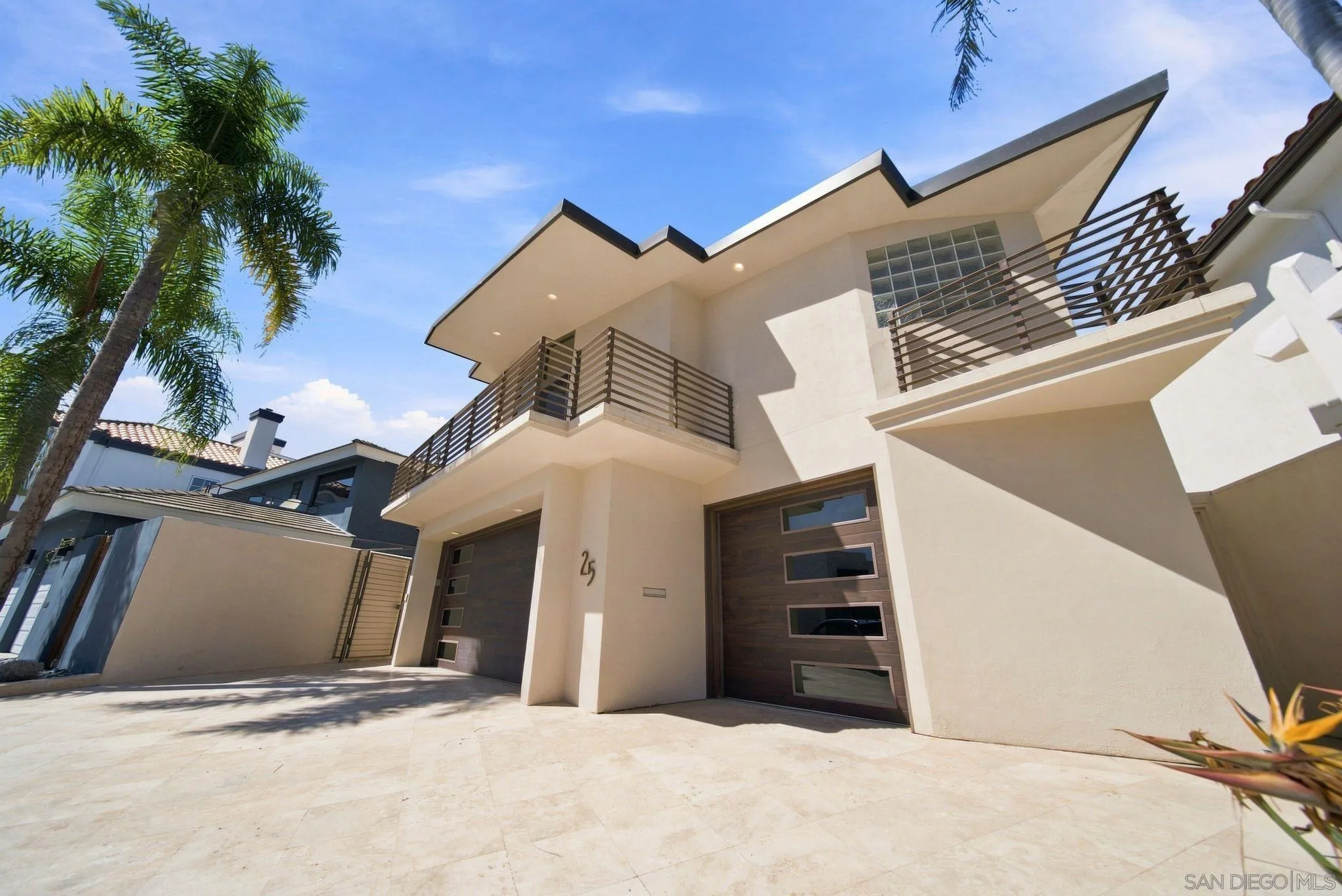 Modern two-story home with angular rooflines, metal-railed balconies, dark garage doors, and a paved driveway.