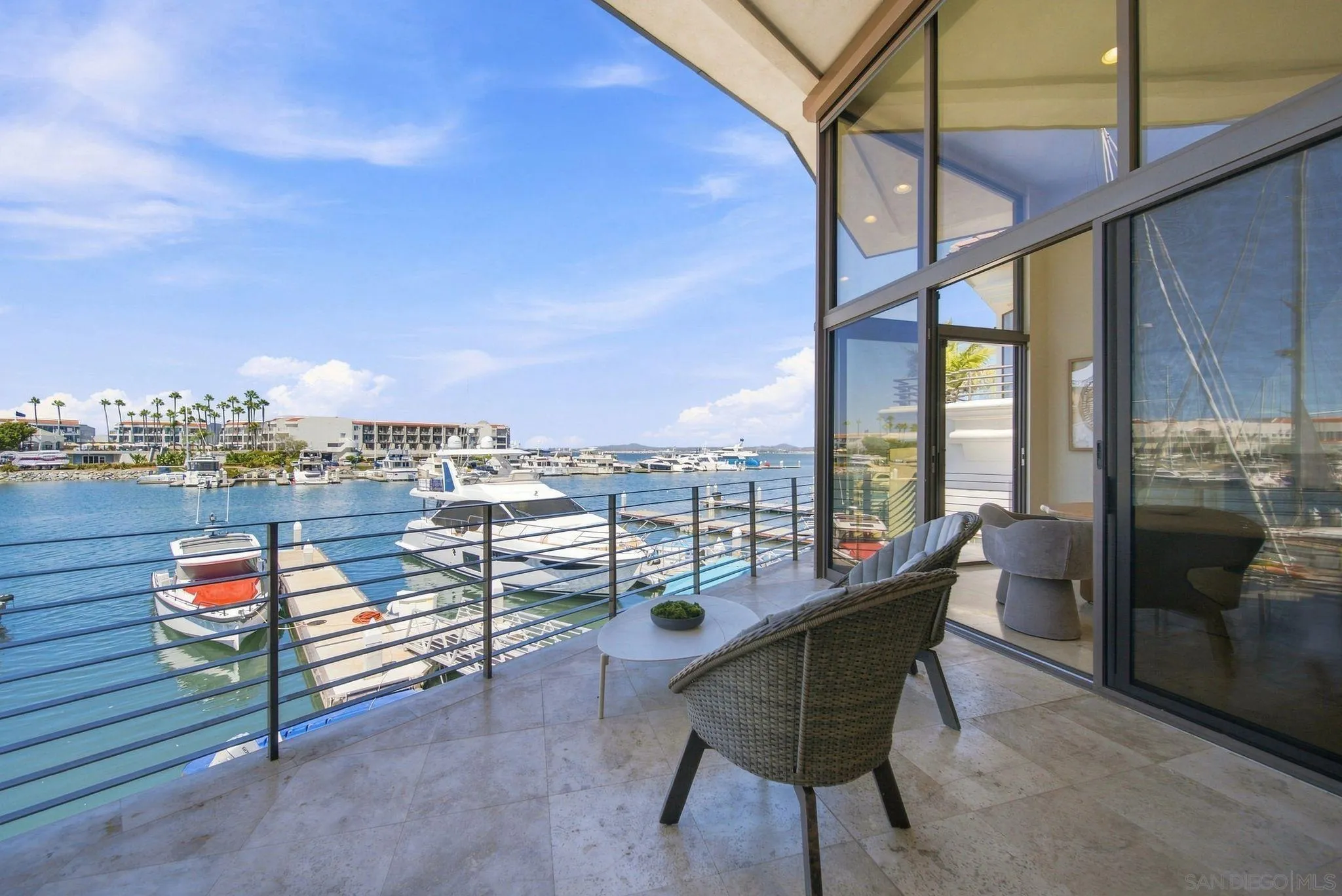 Furnished balcony overlooking a marina, with wicker seating and boats on the water.
