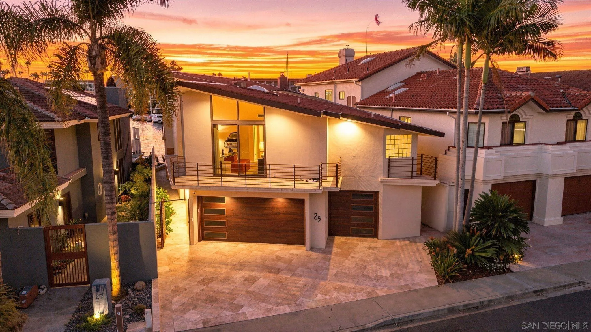 Modern home with tiled driveway and palm trees beneath a vivid sunset sky.