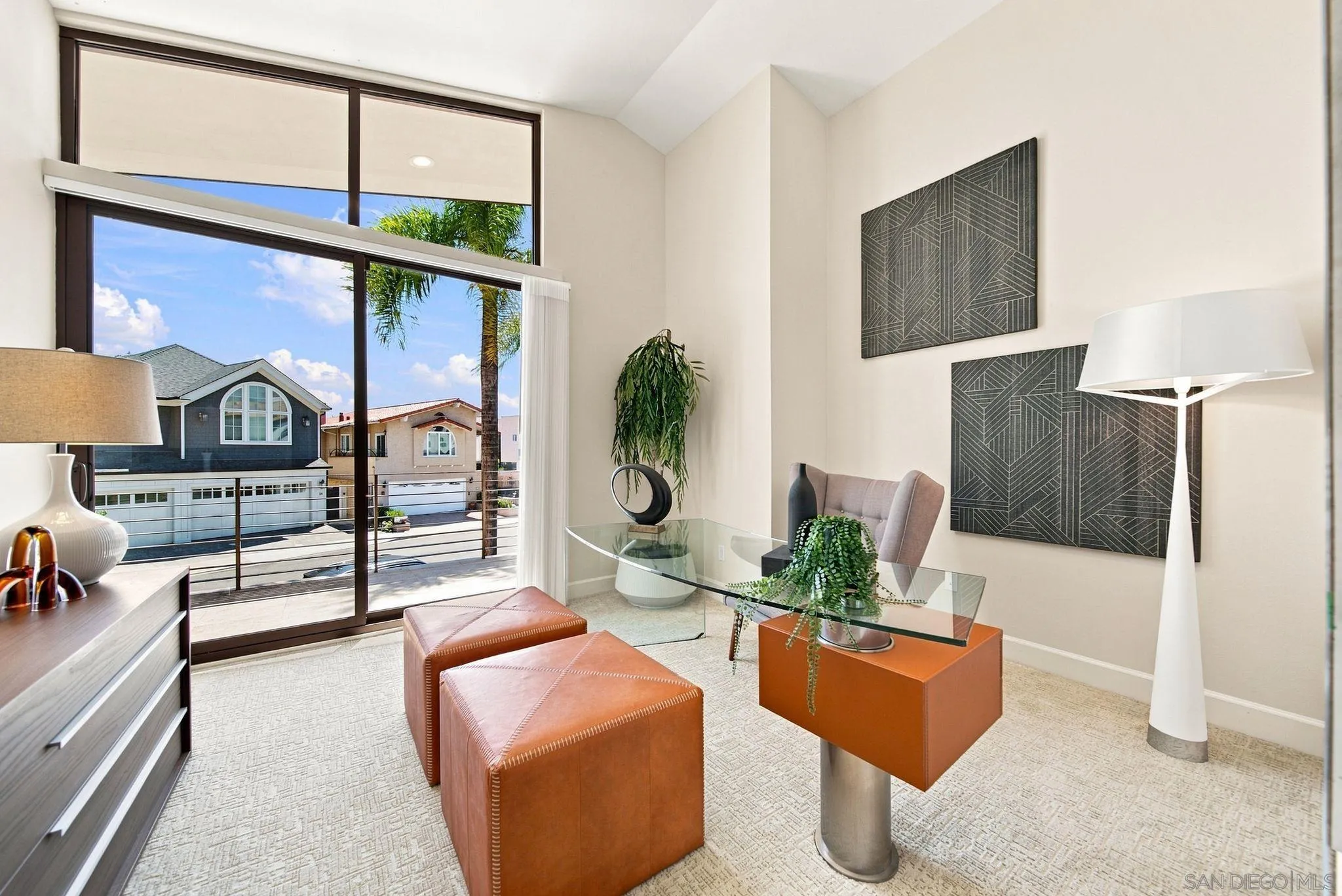Sitting room with a glass desk and leather ottomans beside large sliding doors opening to a balcony.