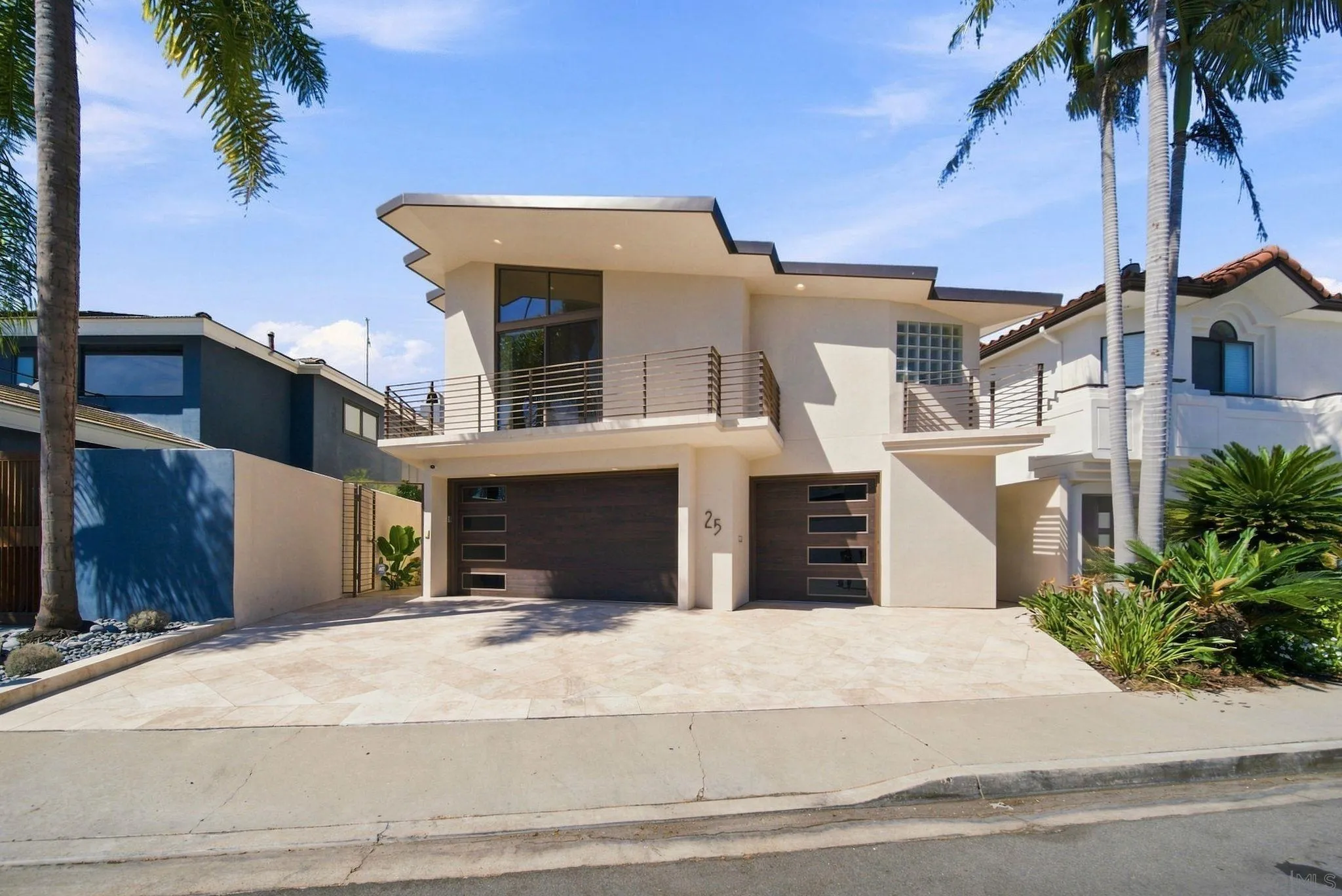 Modern two-story home with two dark garage doors, broad driveway, and palm-framed balconies.