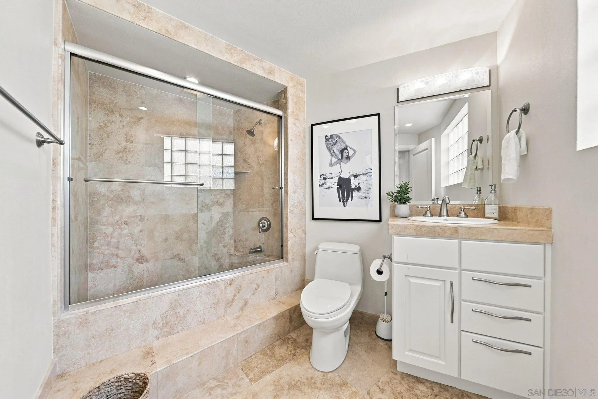 Bathroom with a glass-enclosed stone tub and shower, white toilet, and vanity.