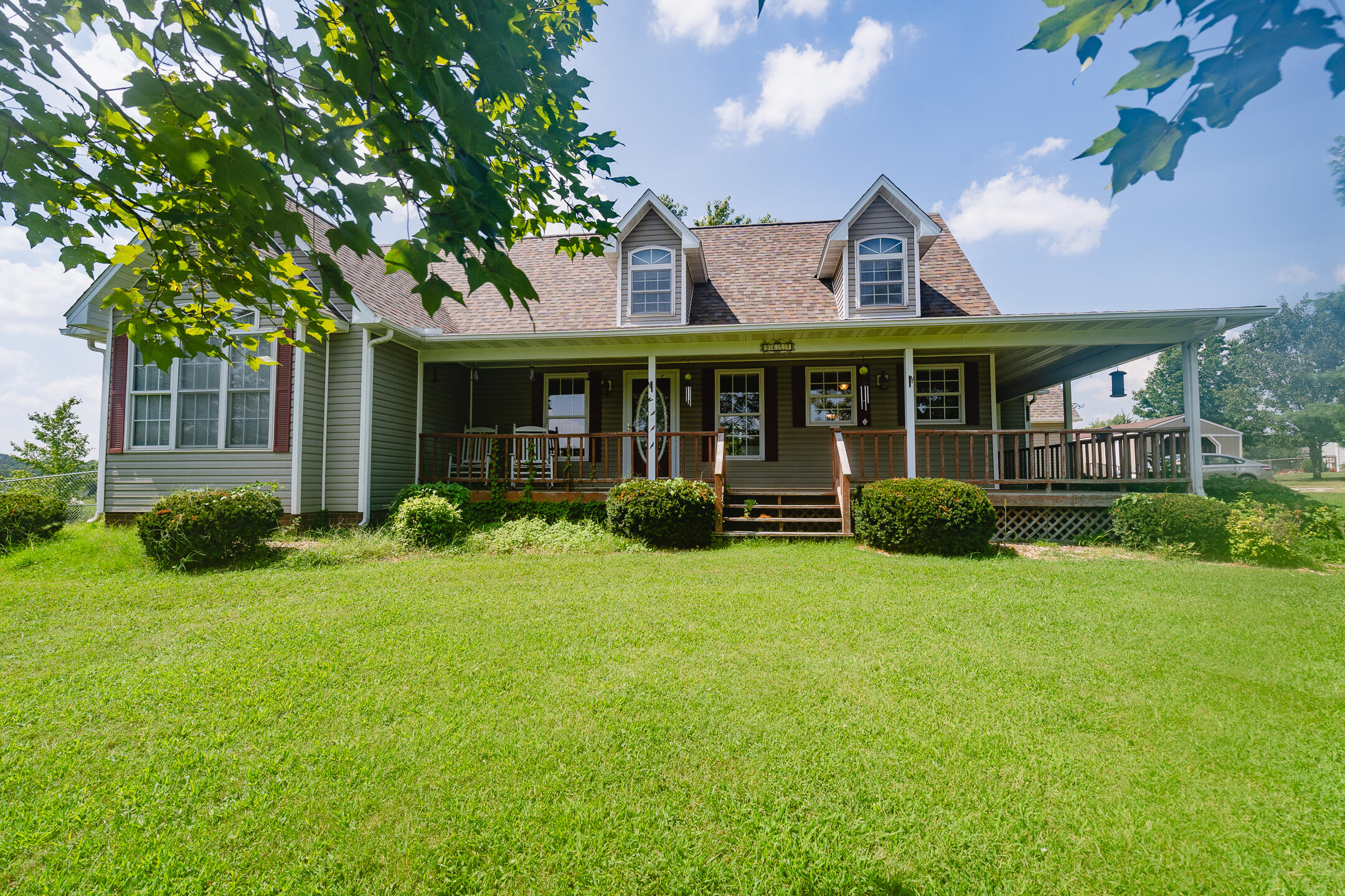Gray-green house with a broad covered porch and dormer windows behind a spacious lawn.