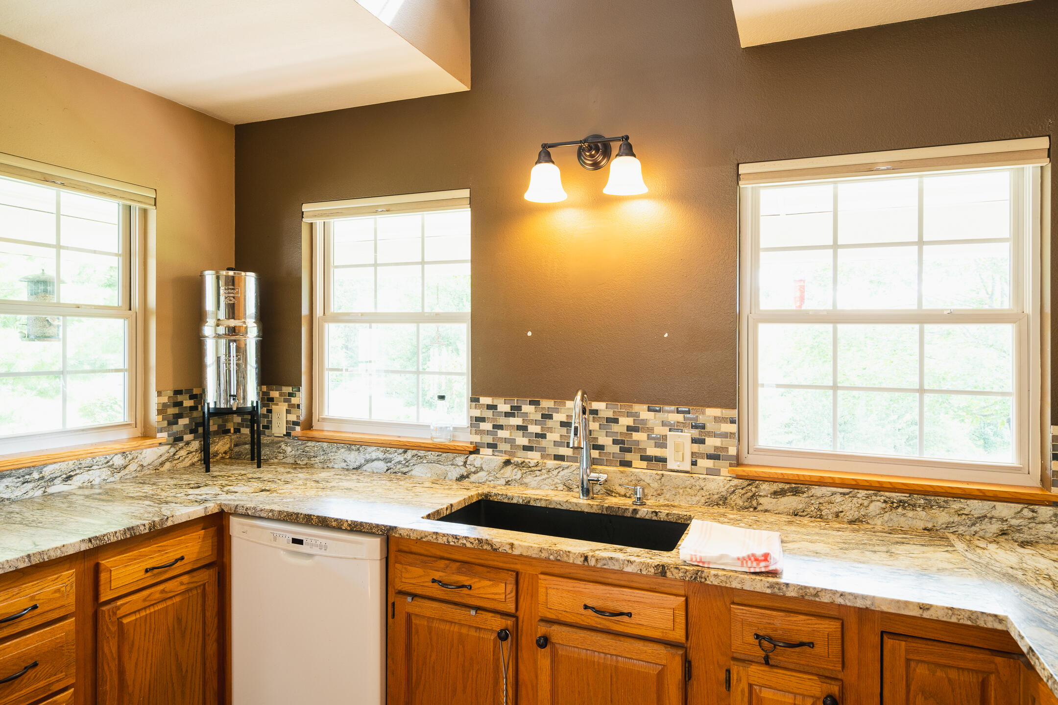 Kitchen with granite counters, warm wood cabinets, a black sink, and three large windows.