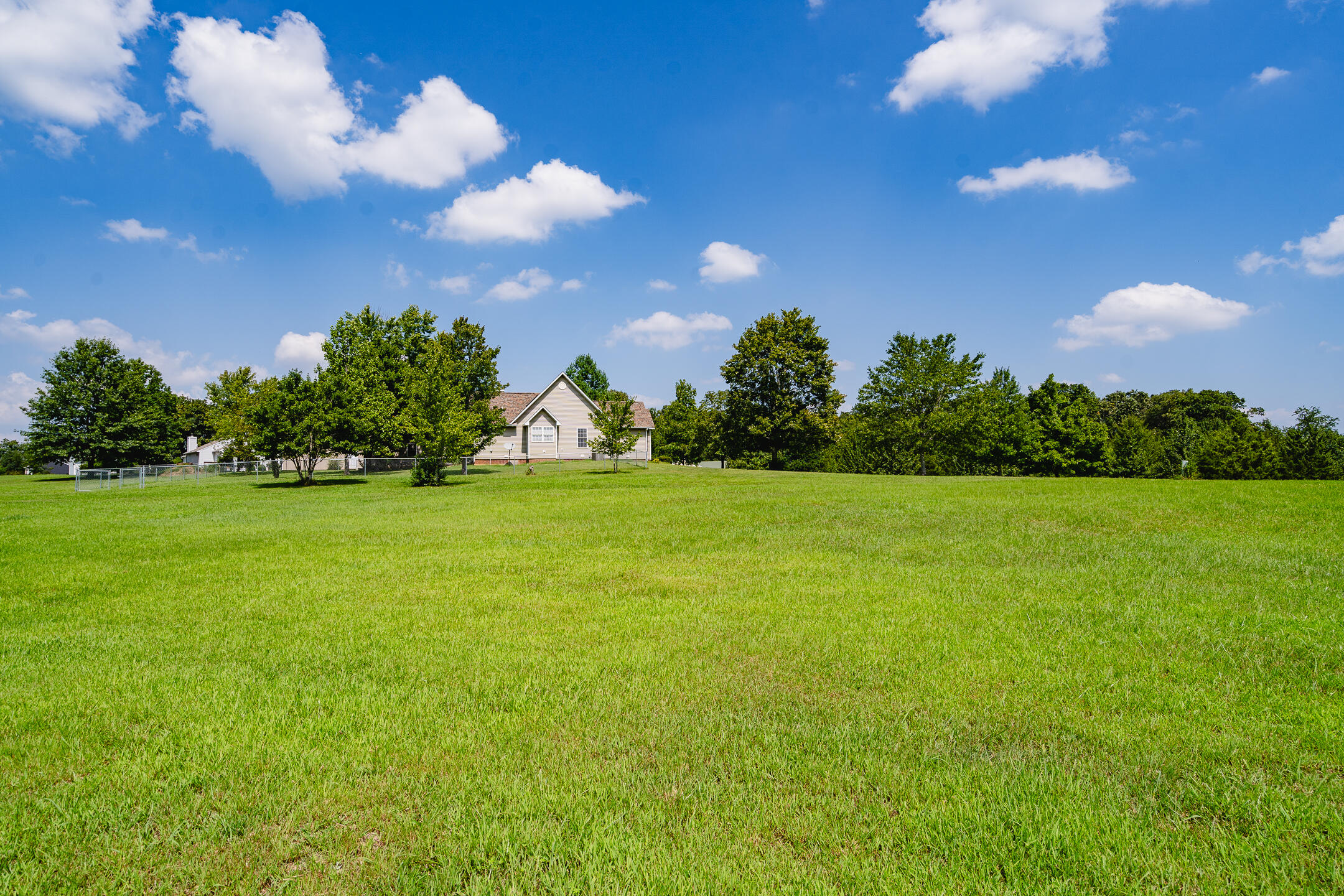 House beyond a broad green lawn, with mature trees and a small fenced area.