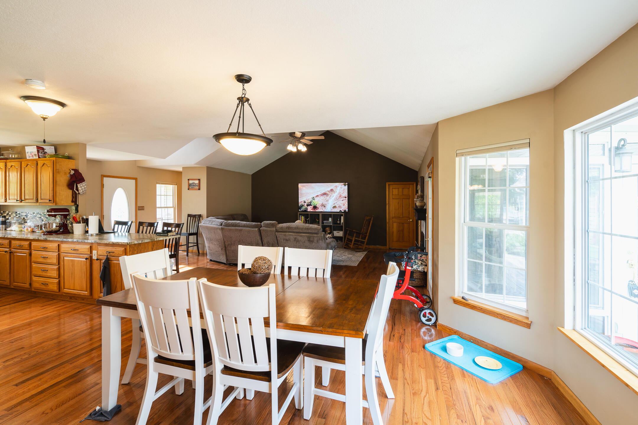 Open-plan dining and living area with a white table, hardwood floors, and a vaulted ceiling.