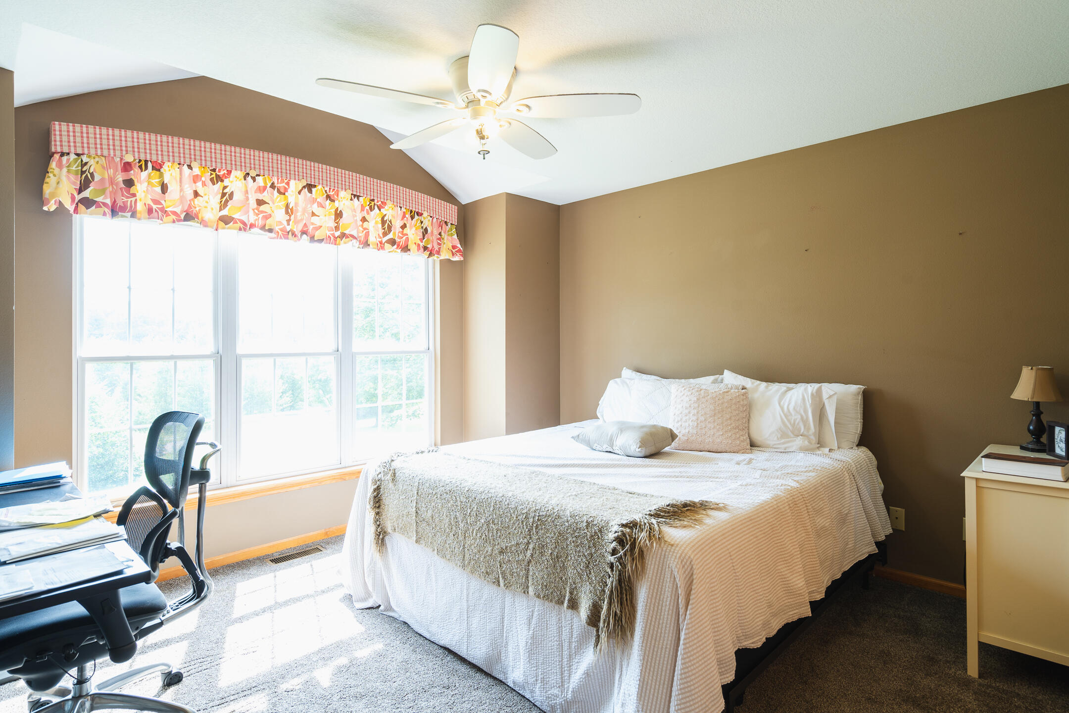 Furnished bedroom with a white bed, large curtained windows, and a ceiling fan.