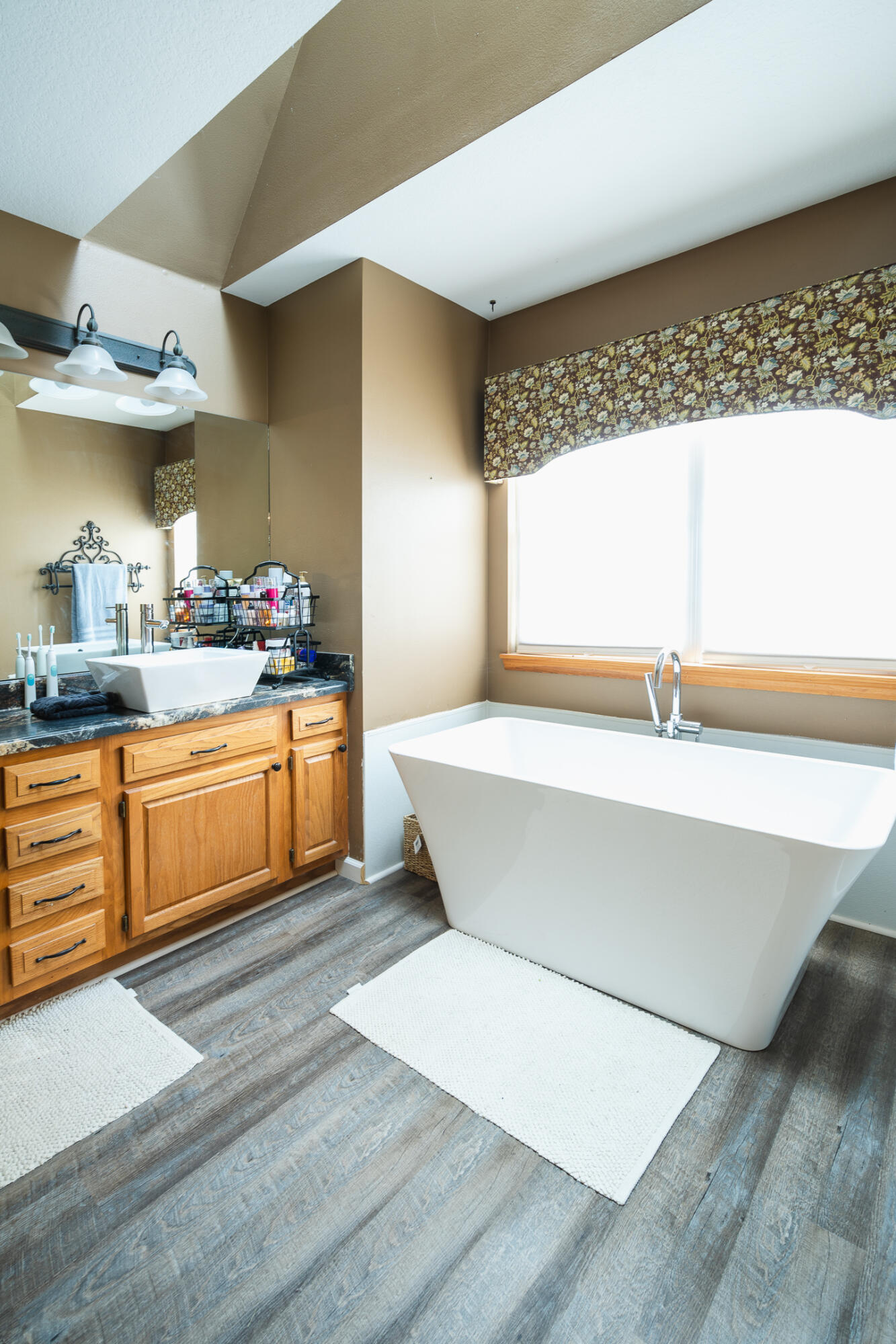 Bathroom with a freestanding tub beside a large window and a wood vanity with vessel sink.