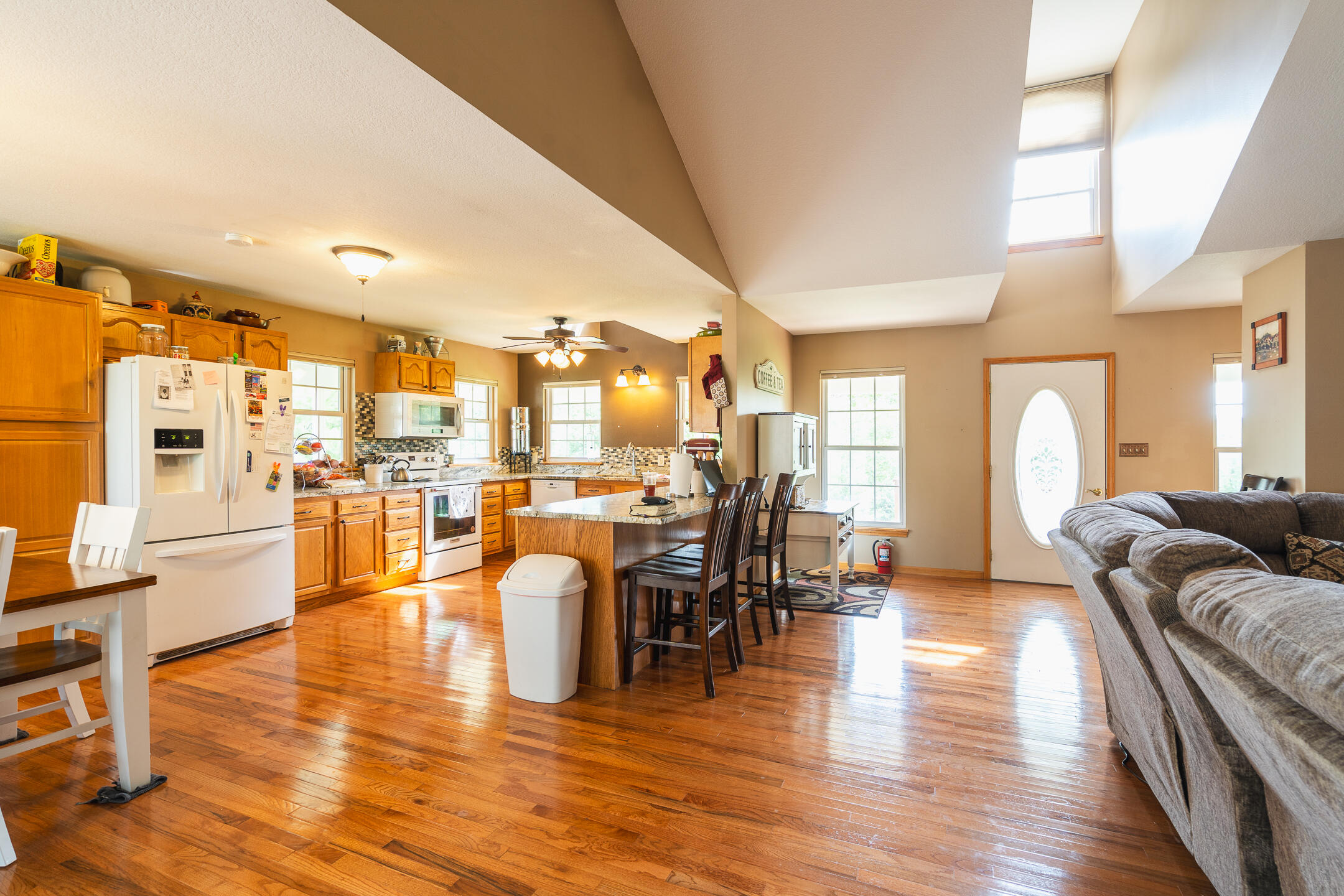Open kitchen and living area with a large island, hardwood floors, vaulted ceiling, and gray sectional sofa.