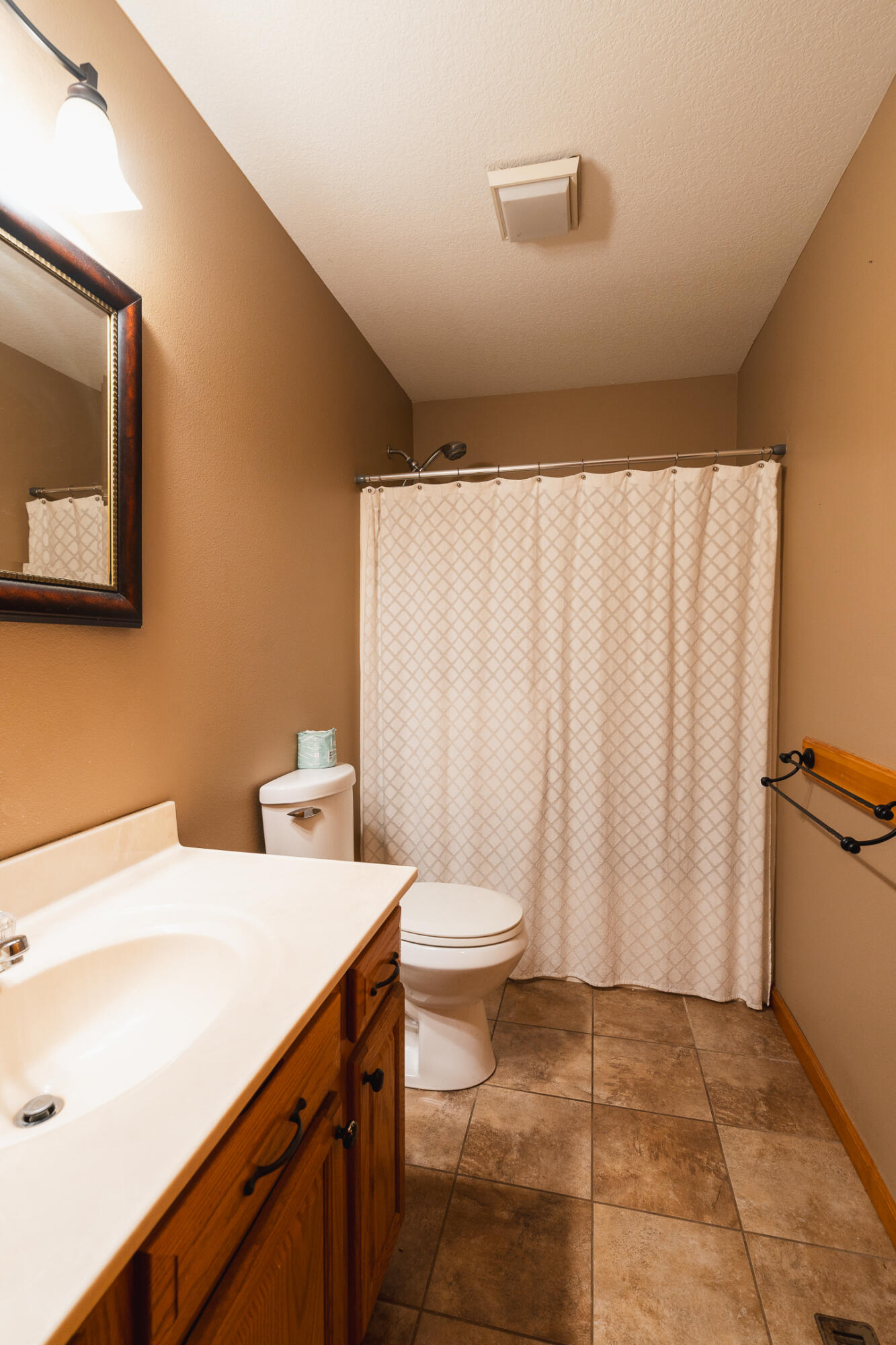 Bathroom with a wood vanity, white patterned shower curtain, and brown tile floor.