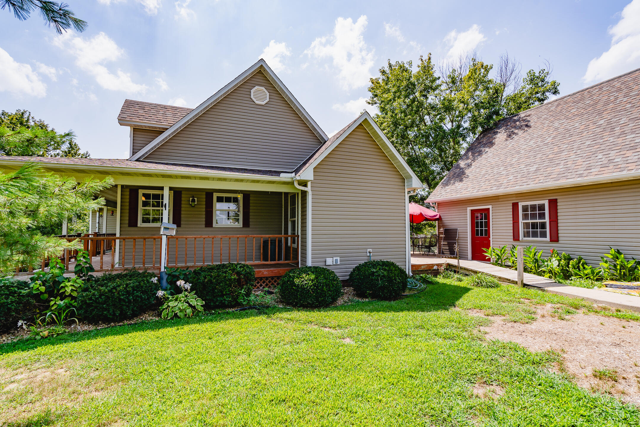 Gray-sided home with a covered porch beside a matching outbuilding with a red door.