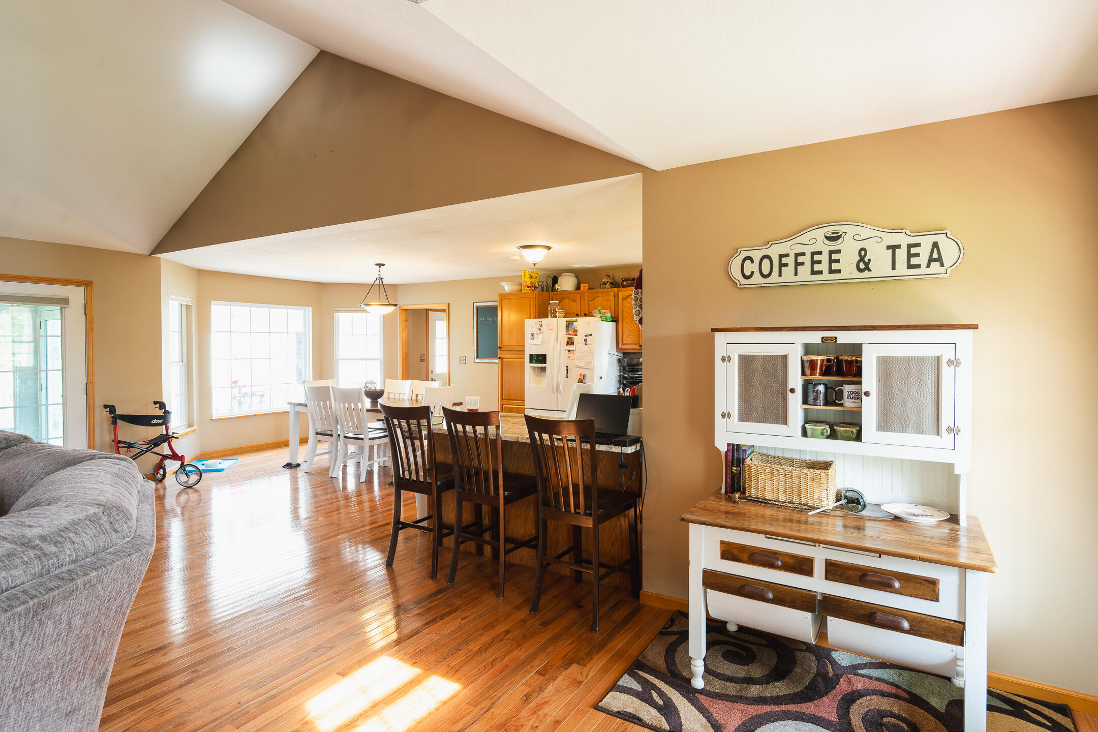 Open-plan living, dining, and kitchen area with vaulted ceiling, hardwood floors, and a coffee station.