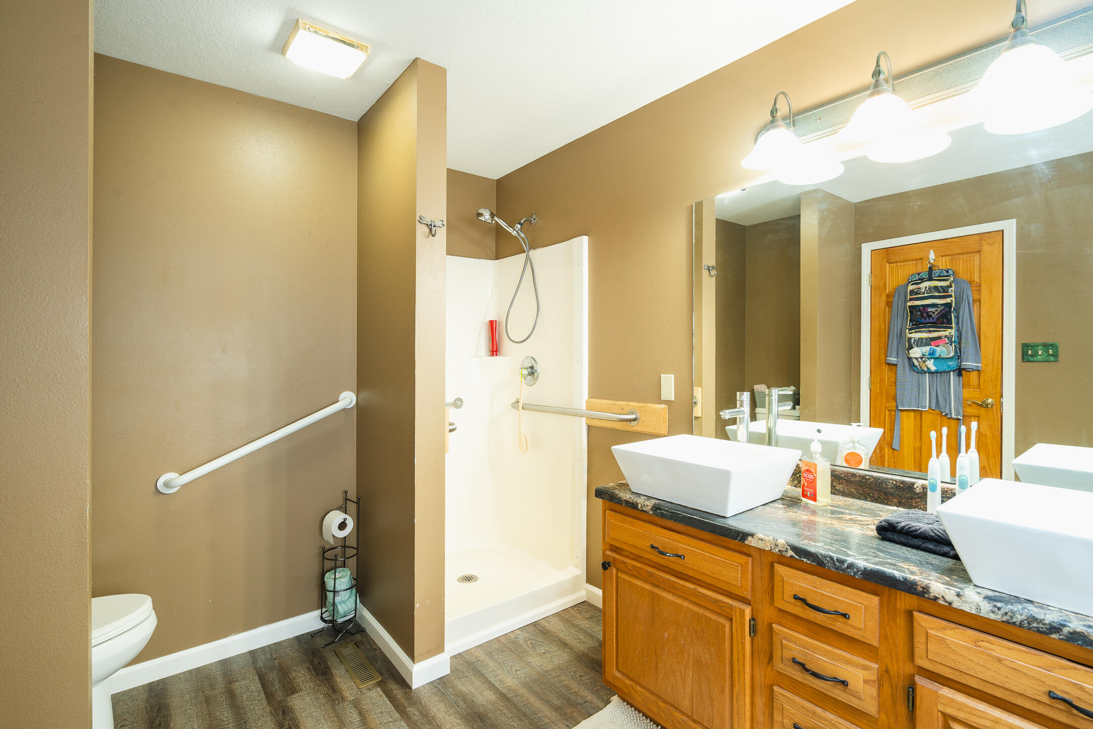 Bathroom with a walk-in shower, grab bars, and a wood vanity with vessel sinks.