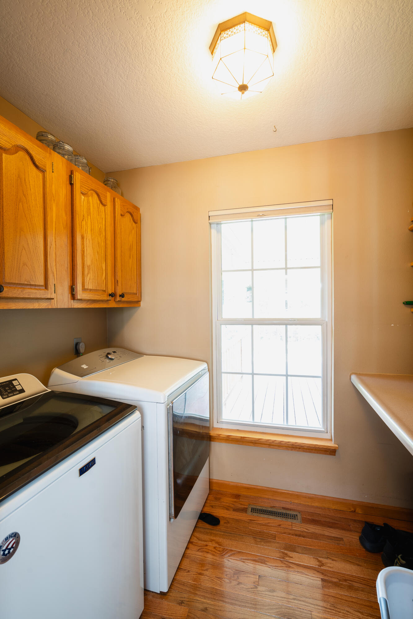 Laundry room with washer and dryer beneath wood cabinets beside a large window.