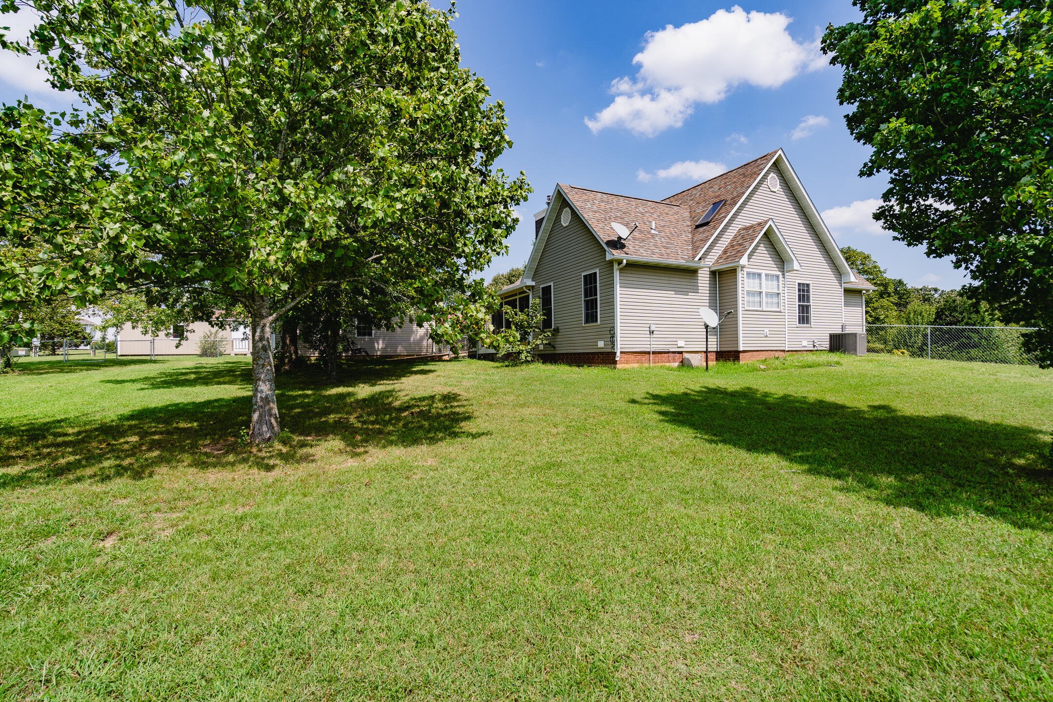 Rear of a gabled home beyond a broad lawn, framed by large shade trees.