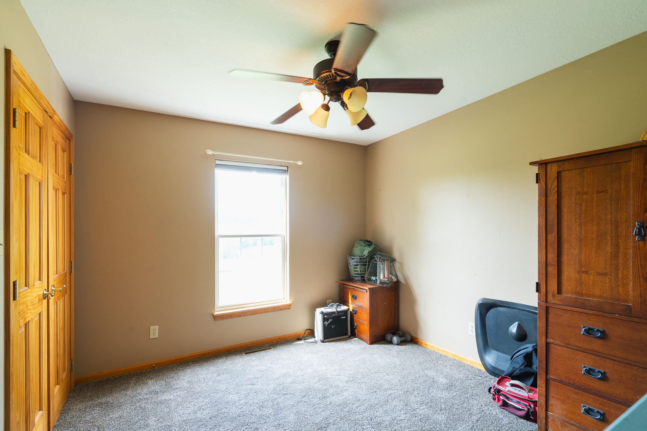 Carpeted bedroom with wooden closet doors, a large dresser, and a ceiling fan with lights.