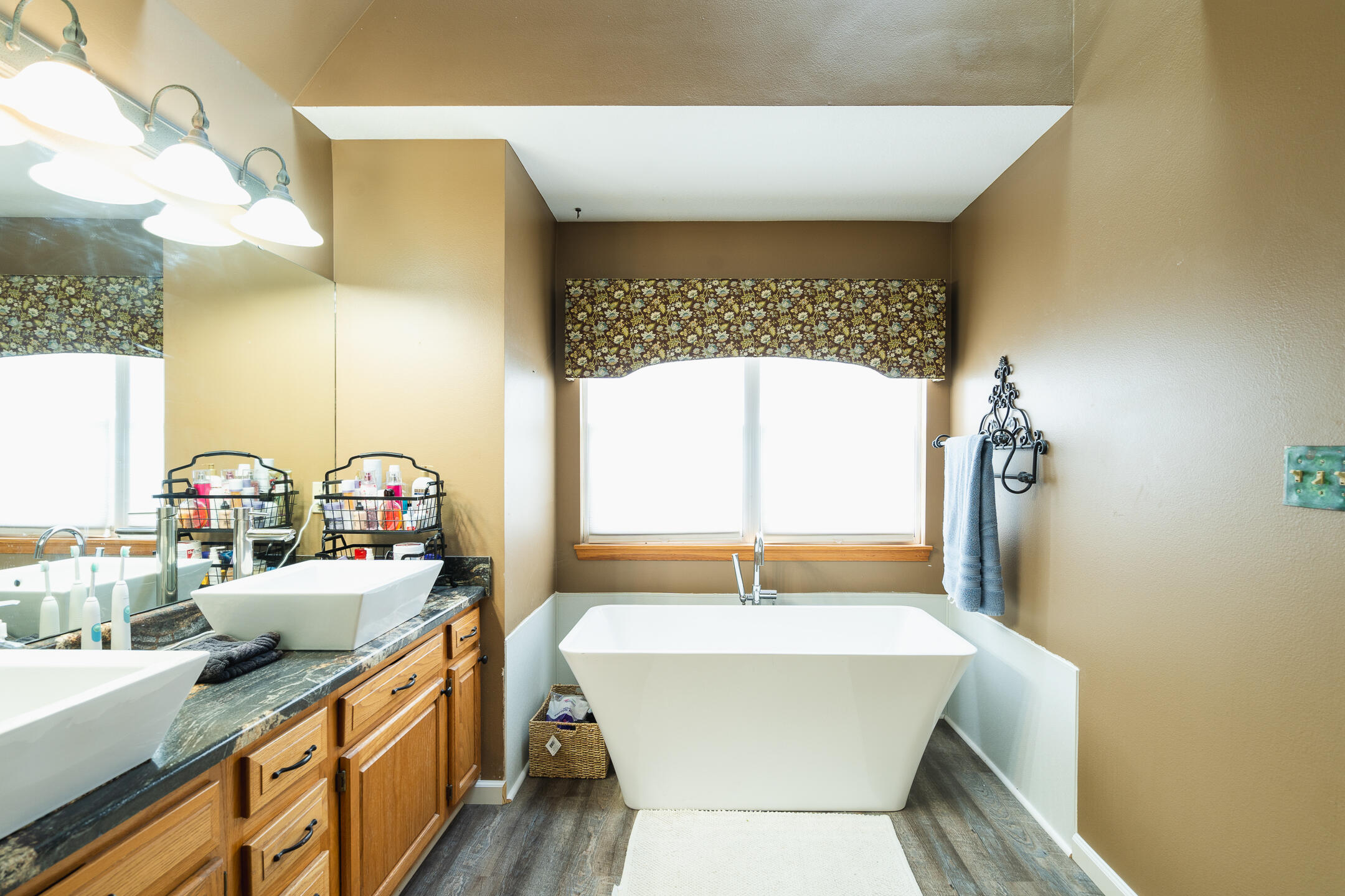 Bathroom with a freestanding tub beneath a floral valance and a wood vanity with a vessel sink.