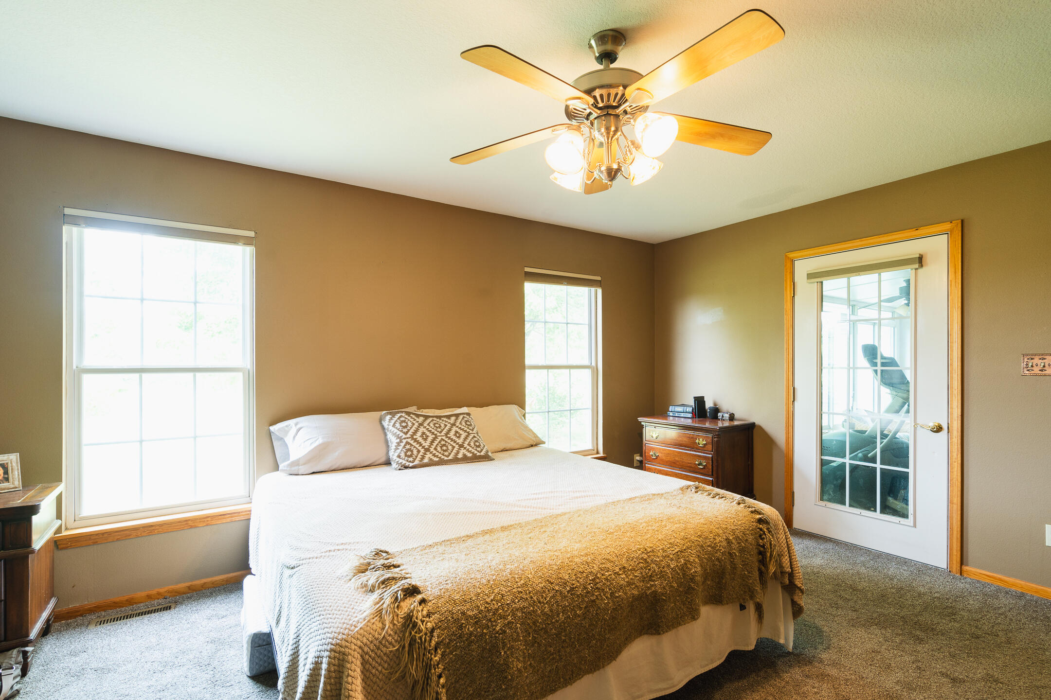 Furnished bedroom with a large bed, two windows, and a ceiling fan with lights.