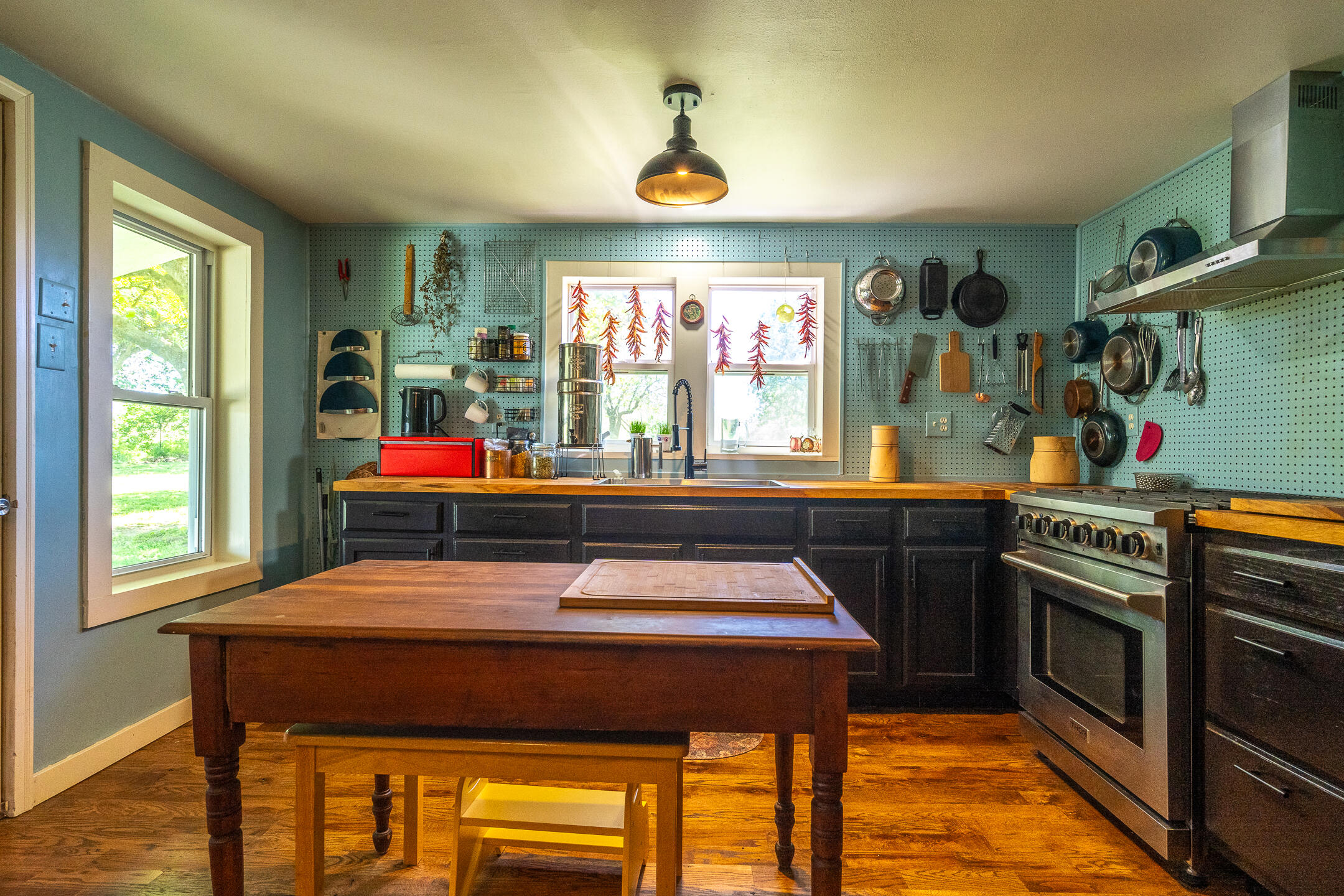 Kitchen with a wooden island, teal pegboard walls, and a stainless-steel range.