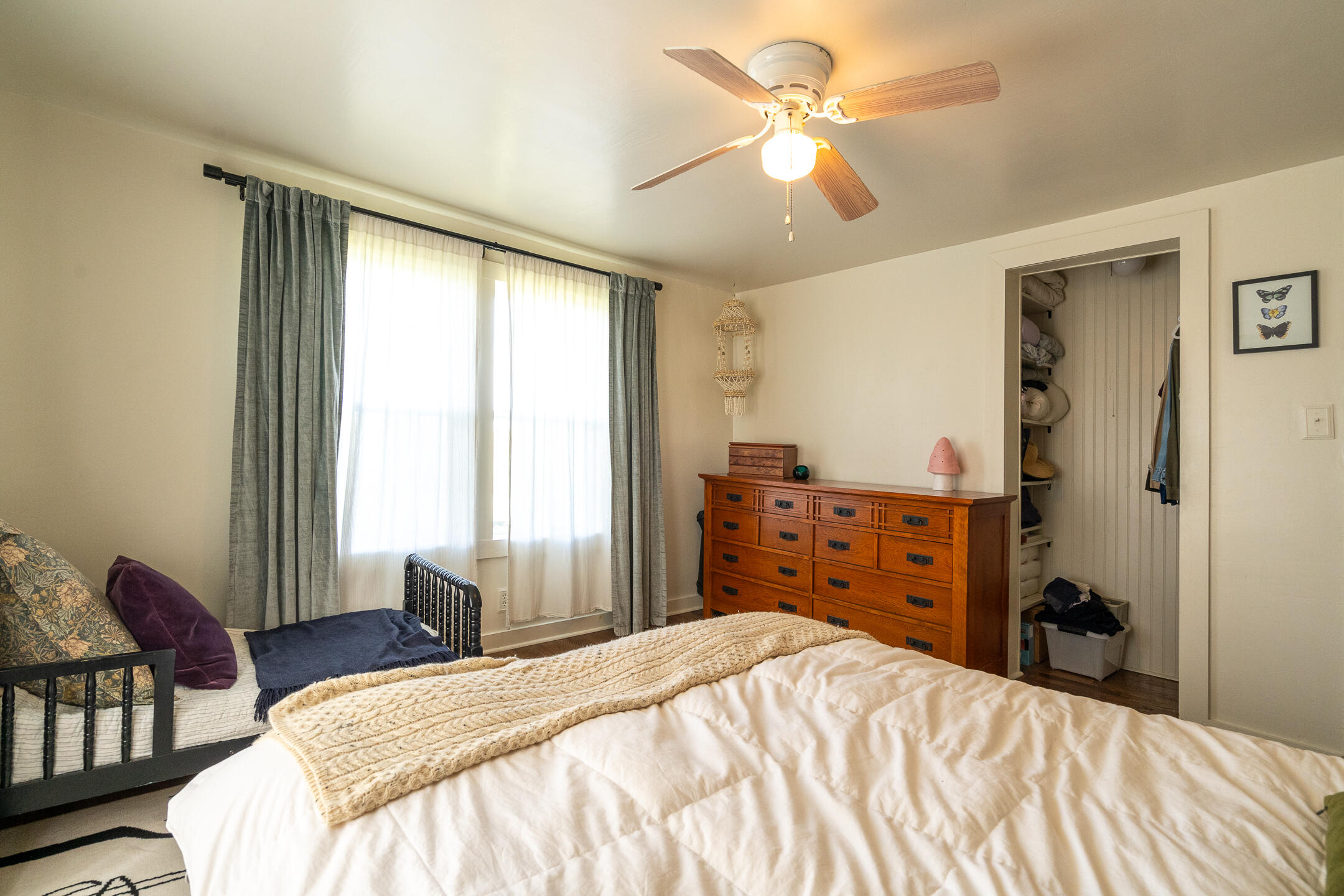 Bedroom with a large white bed, wooden dresser, curtained windows, and an open closet.