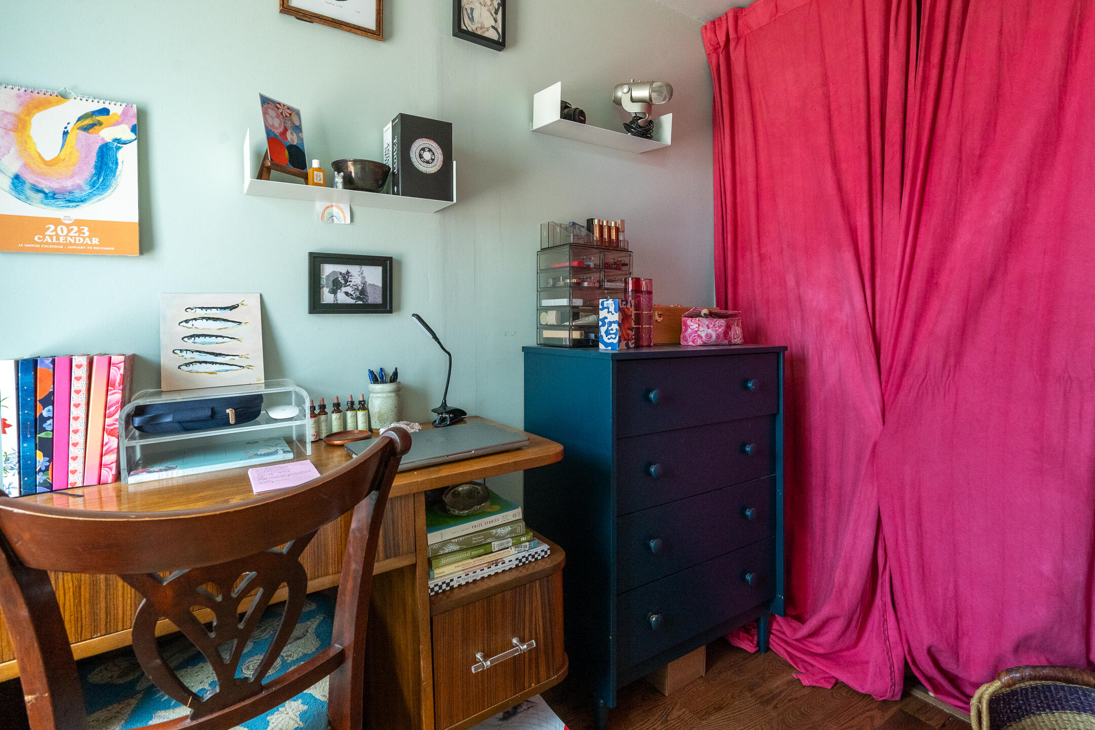 Home office with a wooden desk, dark chest of drawers, and bright magenta curtains.