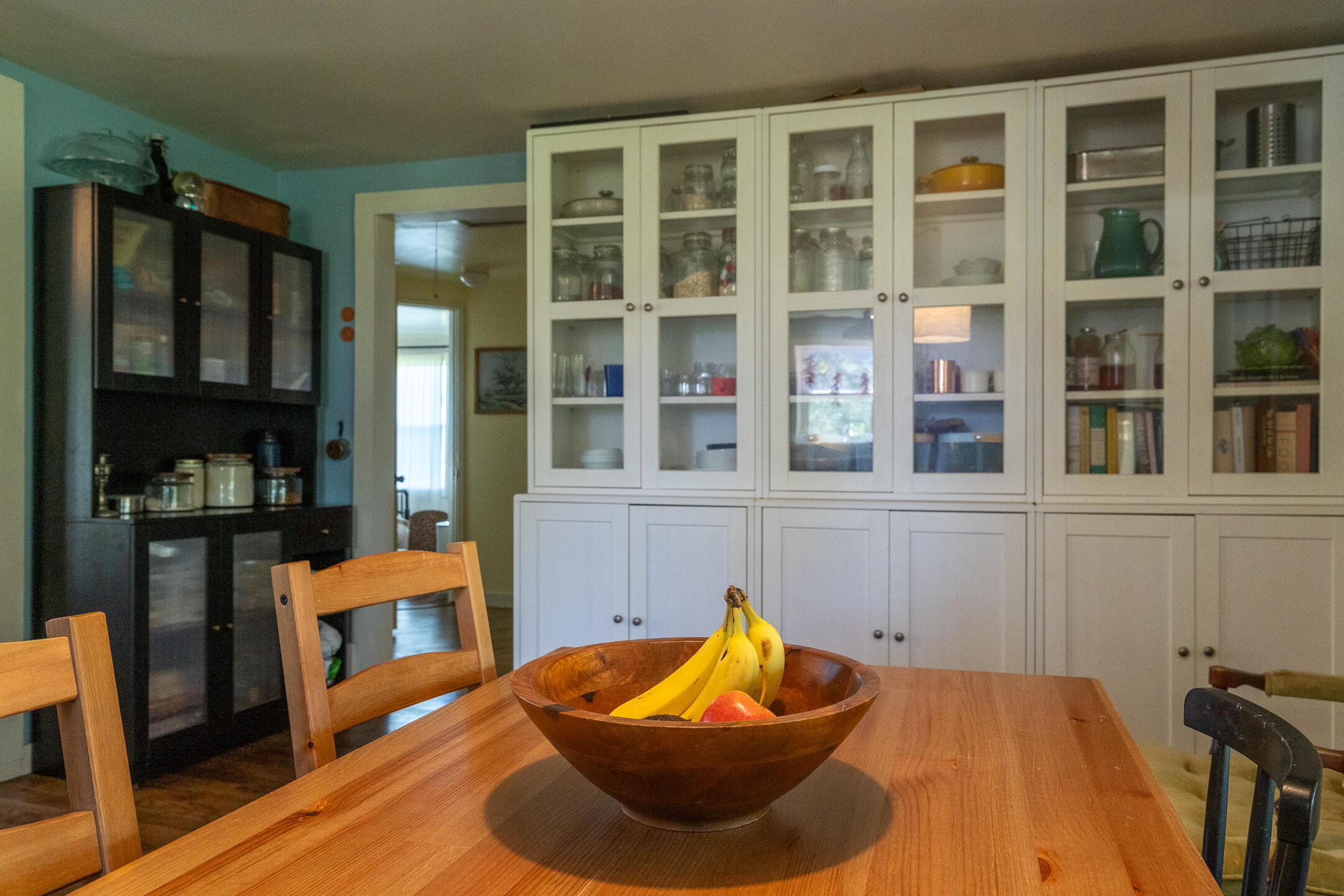 Dining area with a wooden table, fruit bowl, and white glass-front built-in cabinets.