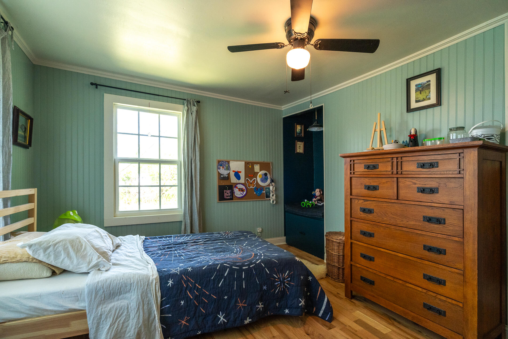 Bedroom with sage-green paneled walls, a patterned bedspread, and a large wooden dresser.