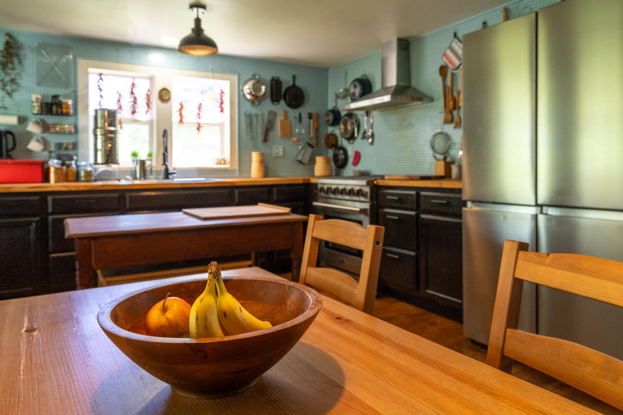 Furnished kitchen with blue-green tile walls, dark cabinets, wooden counters, and a bowl of fruit.