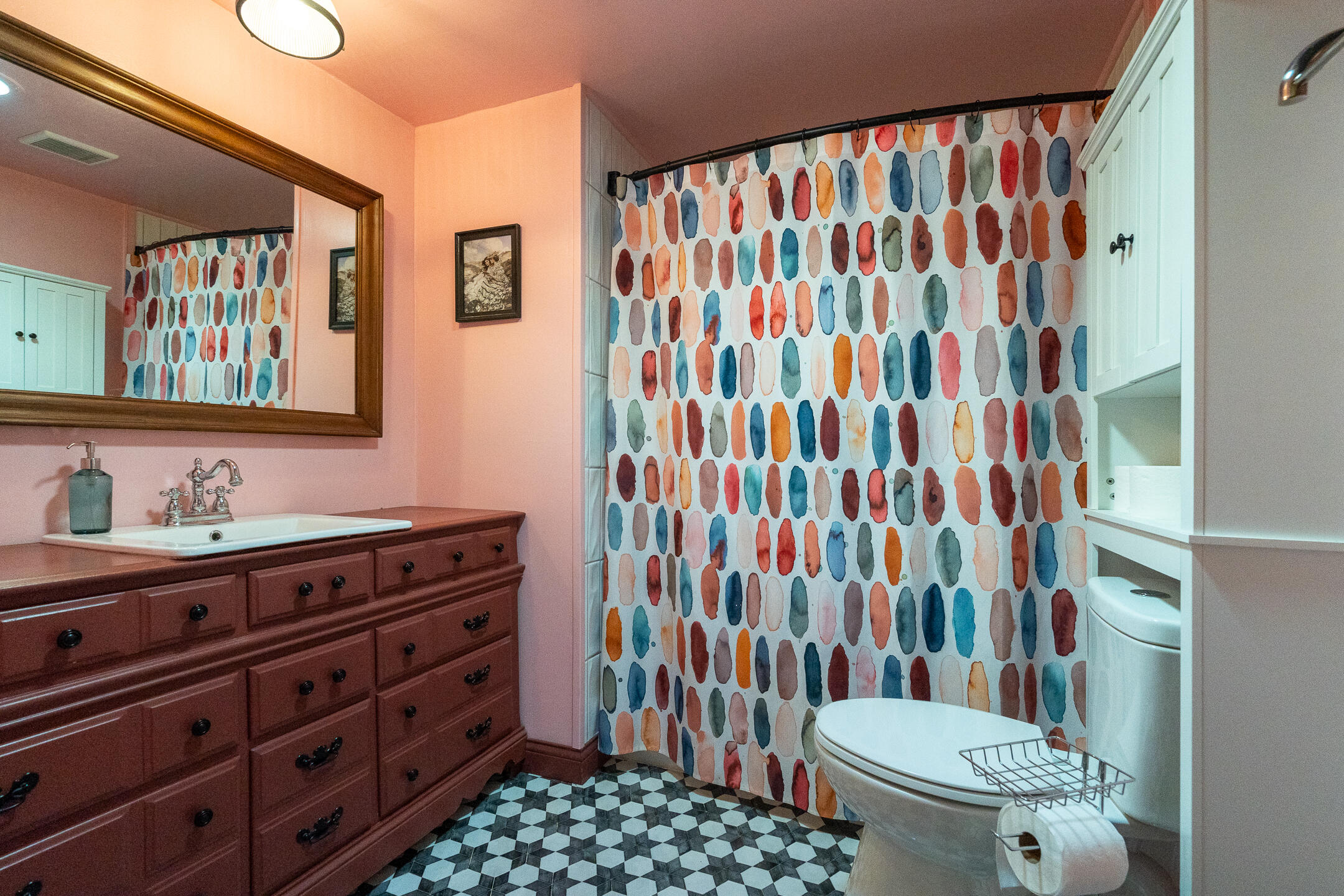 Bathroom with a colorful shower curtain, dark wood vanity, and geometric black-and-white floor tile.