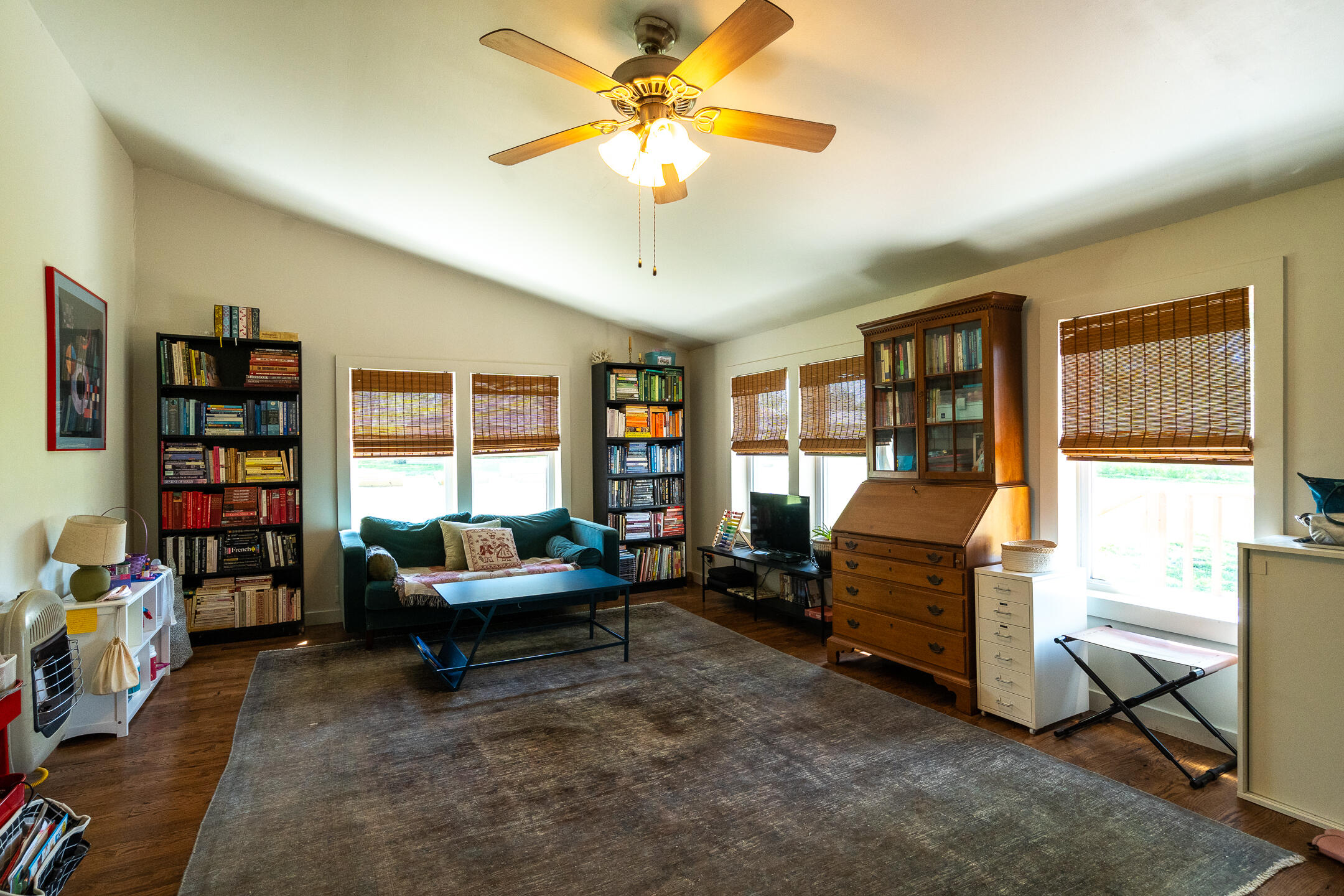 Living room library with bookcases, a teal sofa, wooden secretary desk, and ceiling fan.