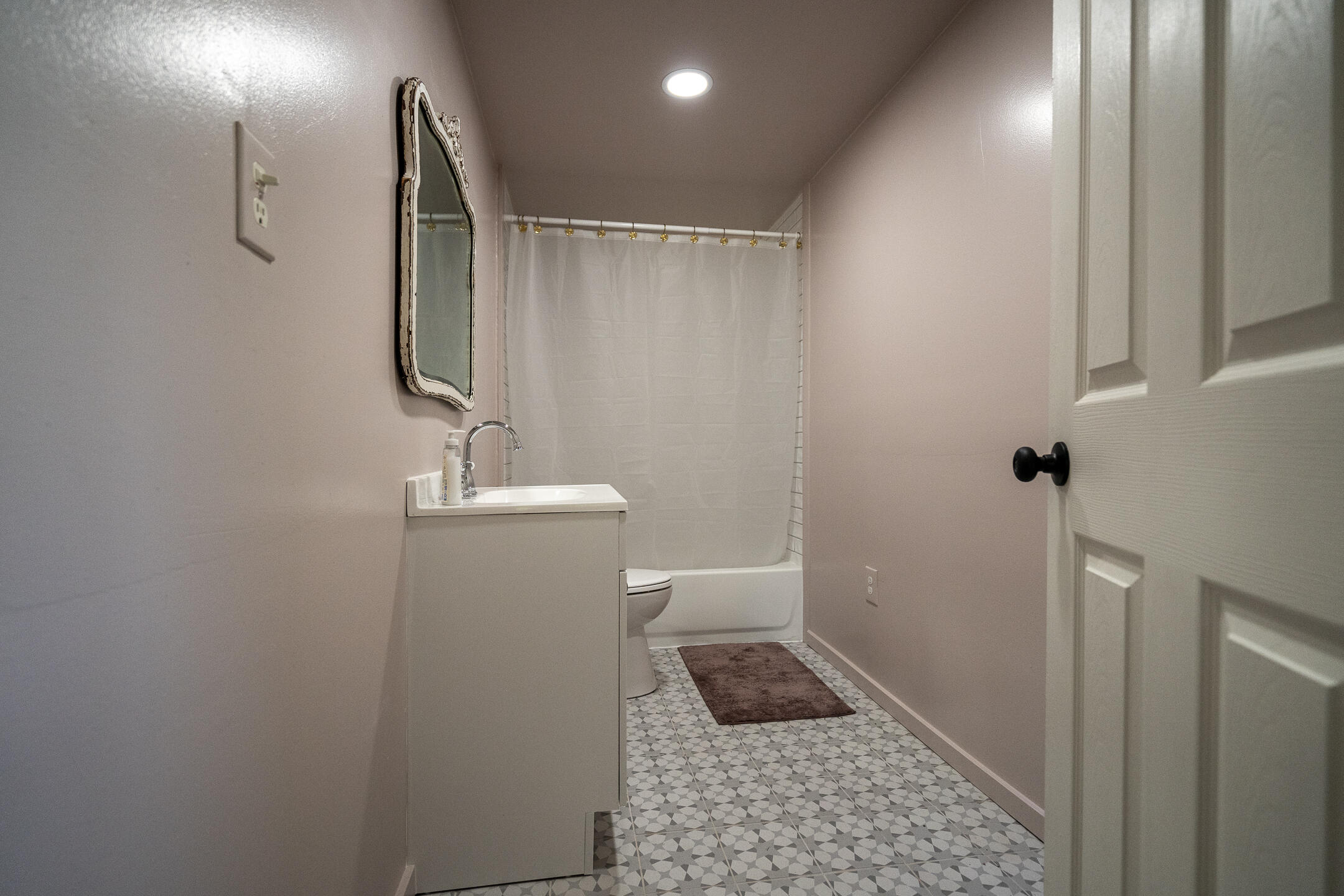 Bathroom with a white vanity, framed mirror, curtained tub, and gray geometric tile floor.
