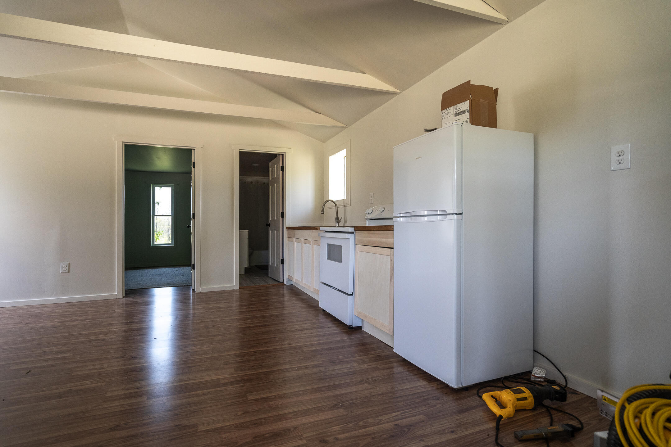 Unfurnished kitchen with white appliances, light cabinets, dark flooring, and tools on the floor.