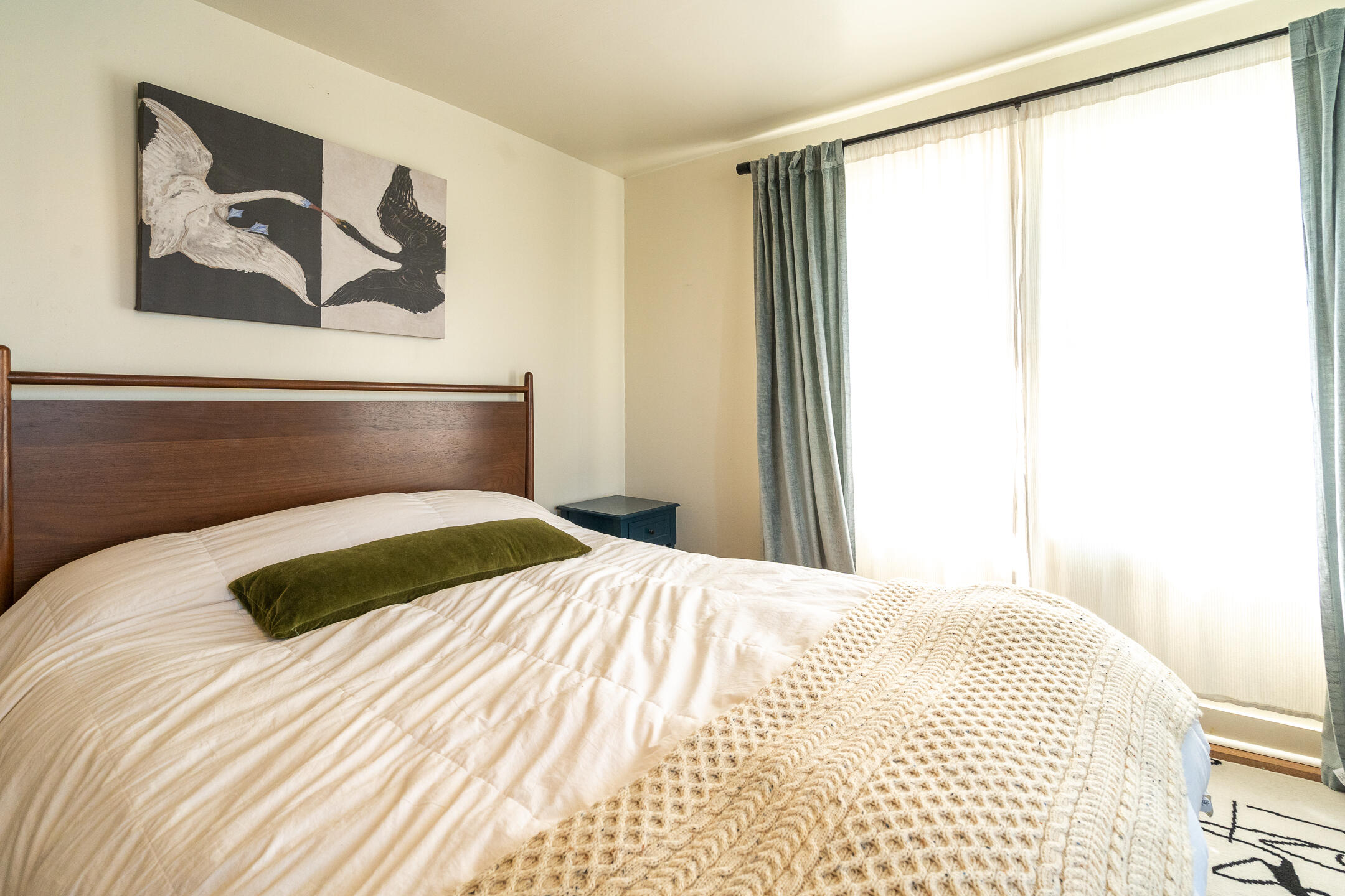 Furnished bedroom with a wooden headboard, bird artwork, and a chunky cream knit blanket.