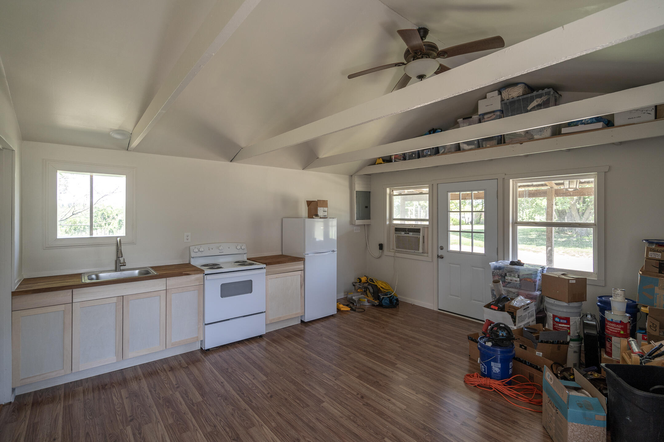Kitchenette with white cabinets, wood-look counters, and a glass exterior door; boxes and tools line one side.