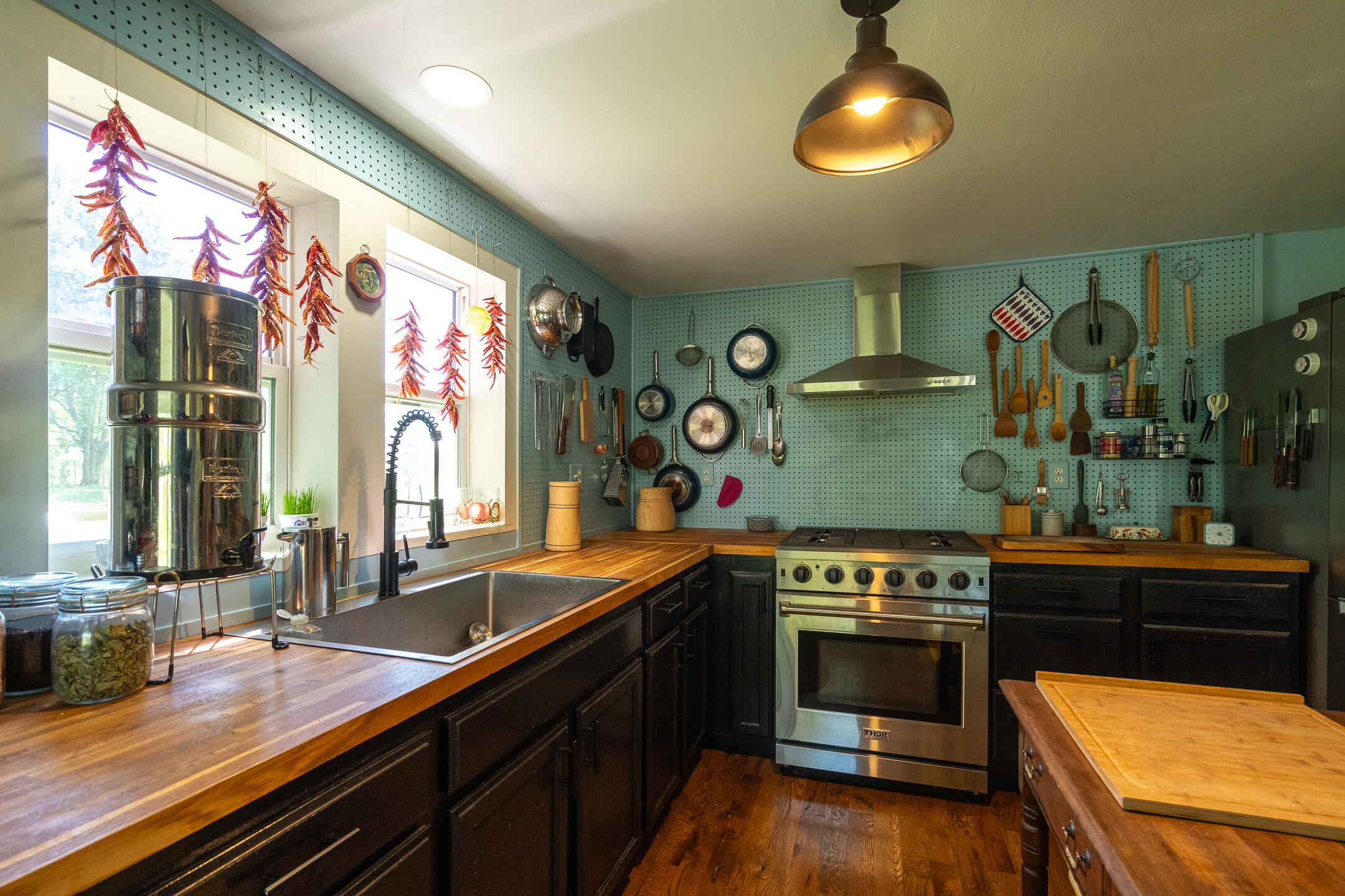 Kitchen with wood countertops, a stainless steel range, and cookware arranged on blue-green pegboard walls.