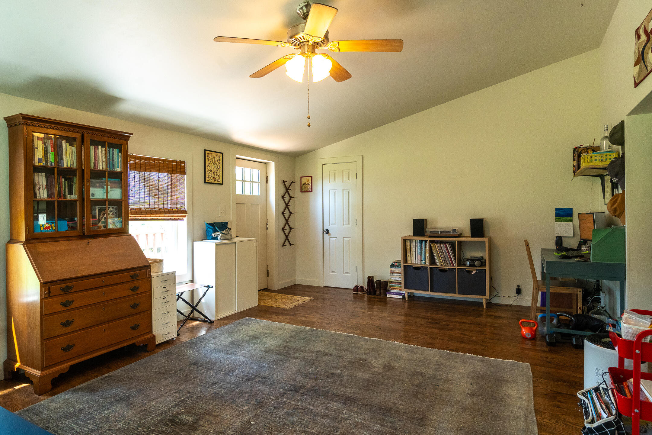 Furnished home office with a wooden secretary desk, bookshelves, dark wood floors, and a large gray rug.