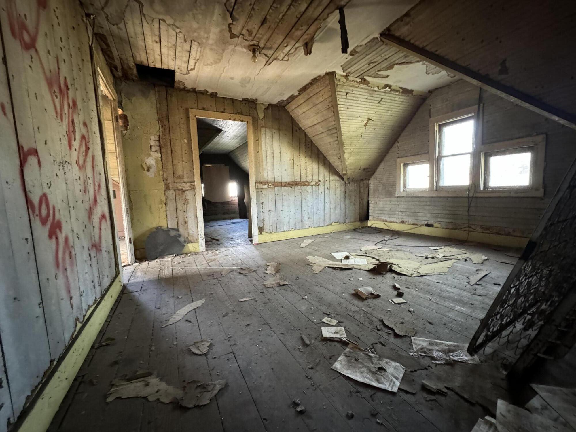 Vacant attic room with sloped ceilings, peeling walls, and debris across the floor.