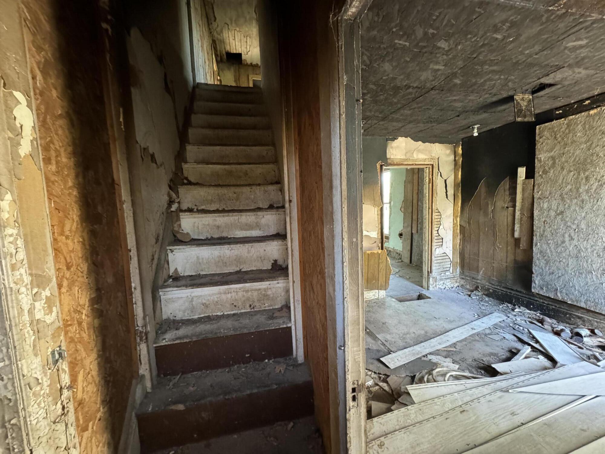 A damaged staircase beside a debris-filled room with peeling walls and exposed ceiling material.