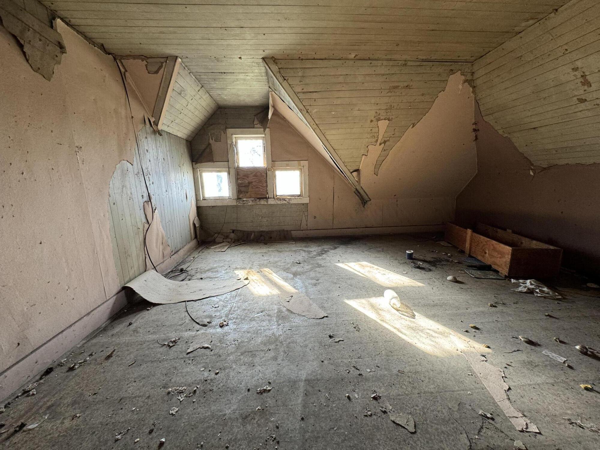 Damaged attic room with peeling walls, a sloped wood ceiling, and debris across the floor.