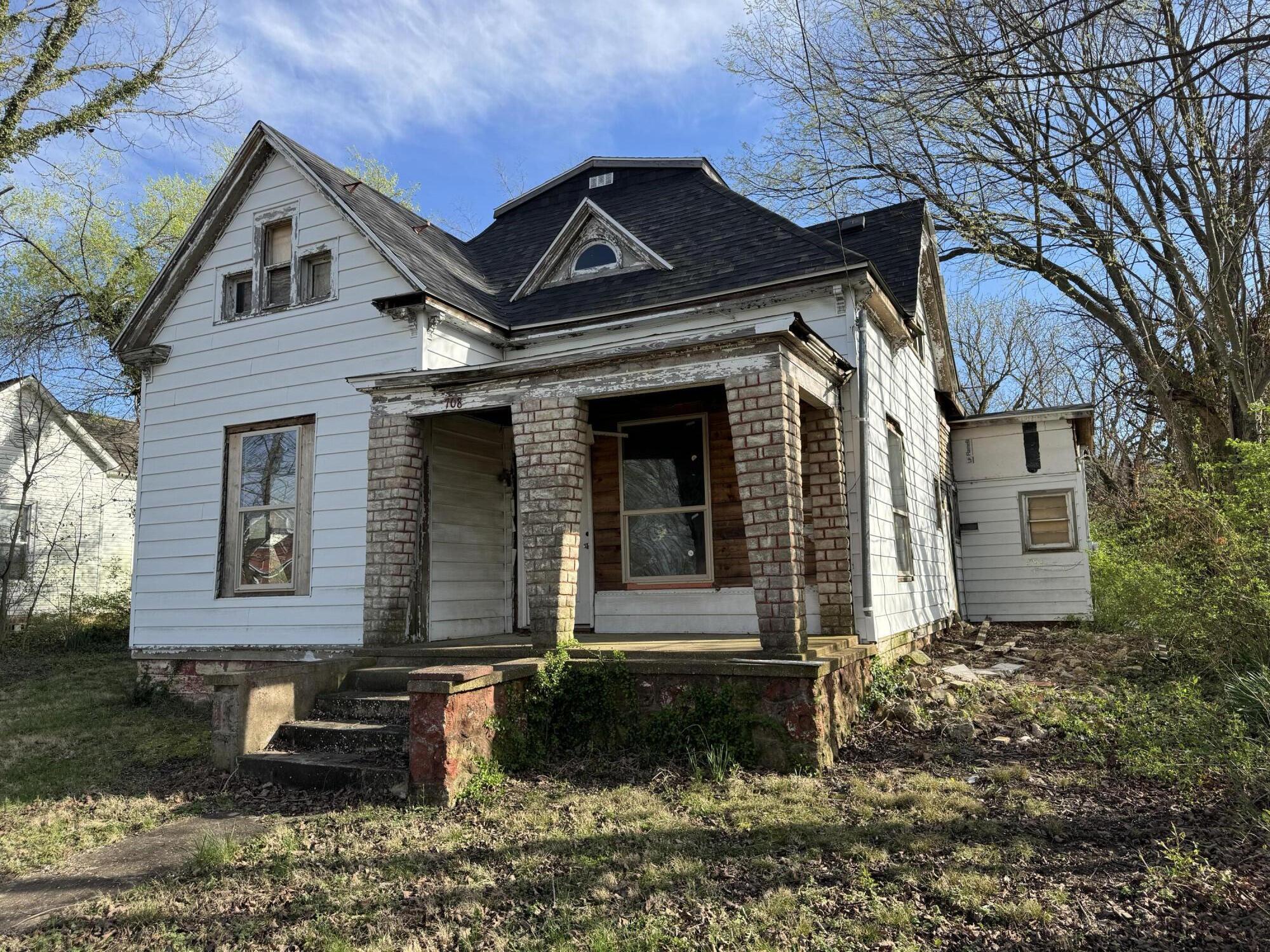 White-sided two-story house with a steep dark roof and brick-column front porch.