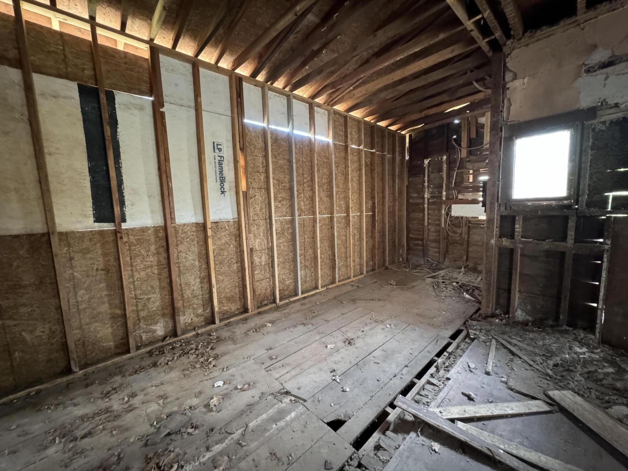 Unfinished interior with exposed framing, roof rafters, and damaged, debris-covered flooring.