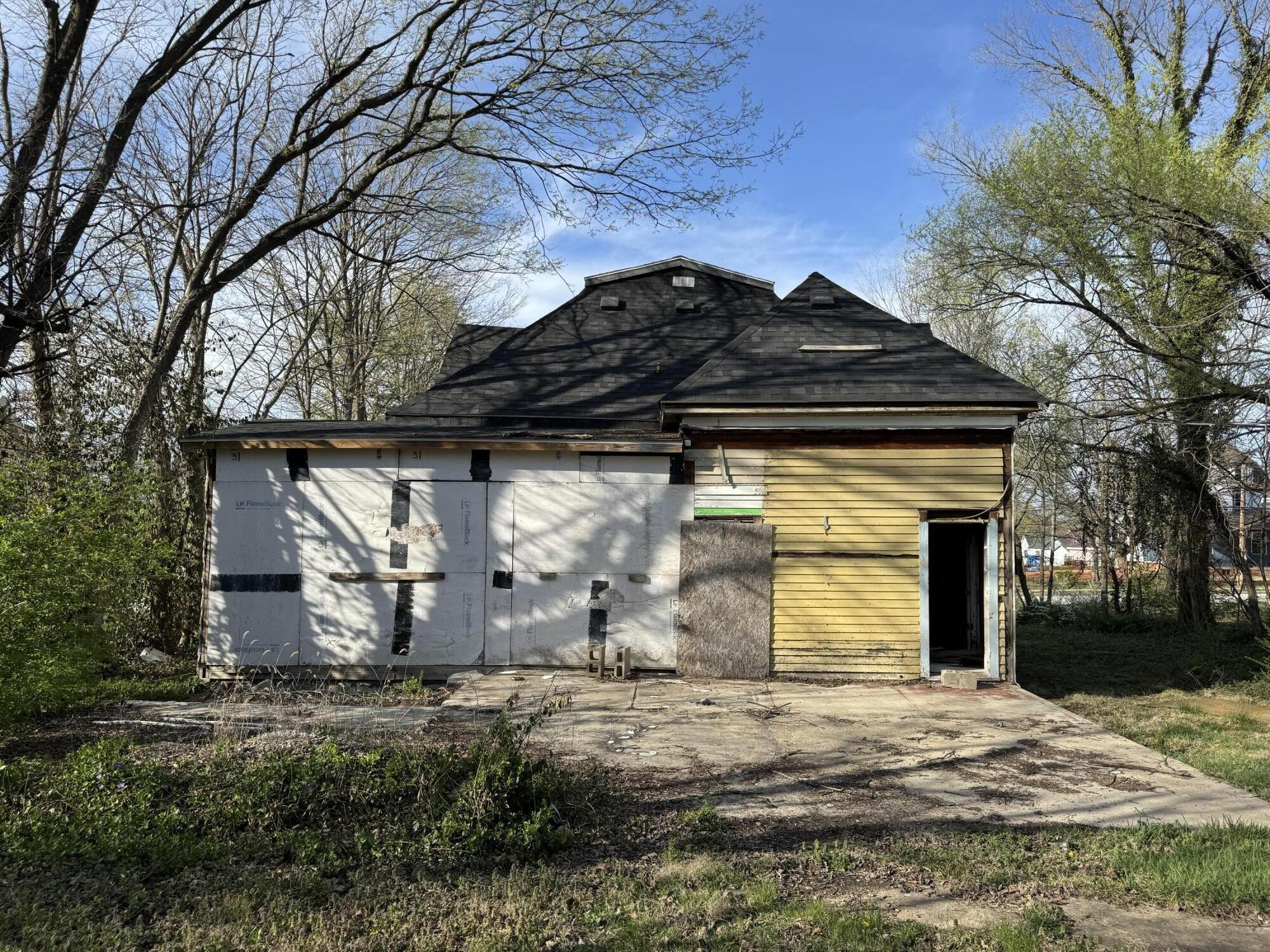 House exterior under renovation, with exposed wall sheathing, partial yellow siding, and a concrete driveway.
