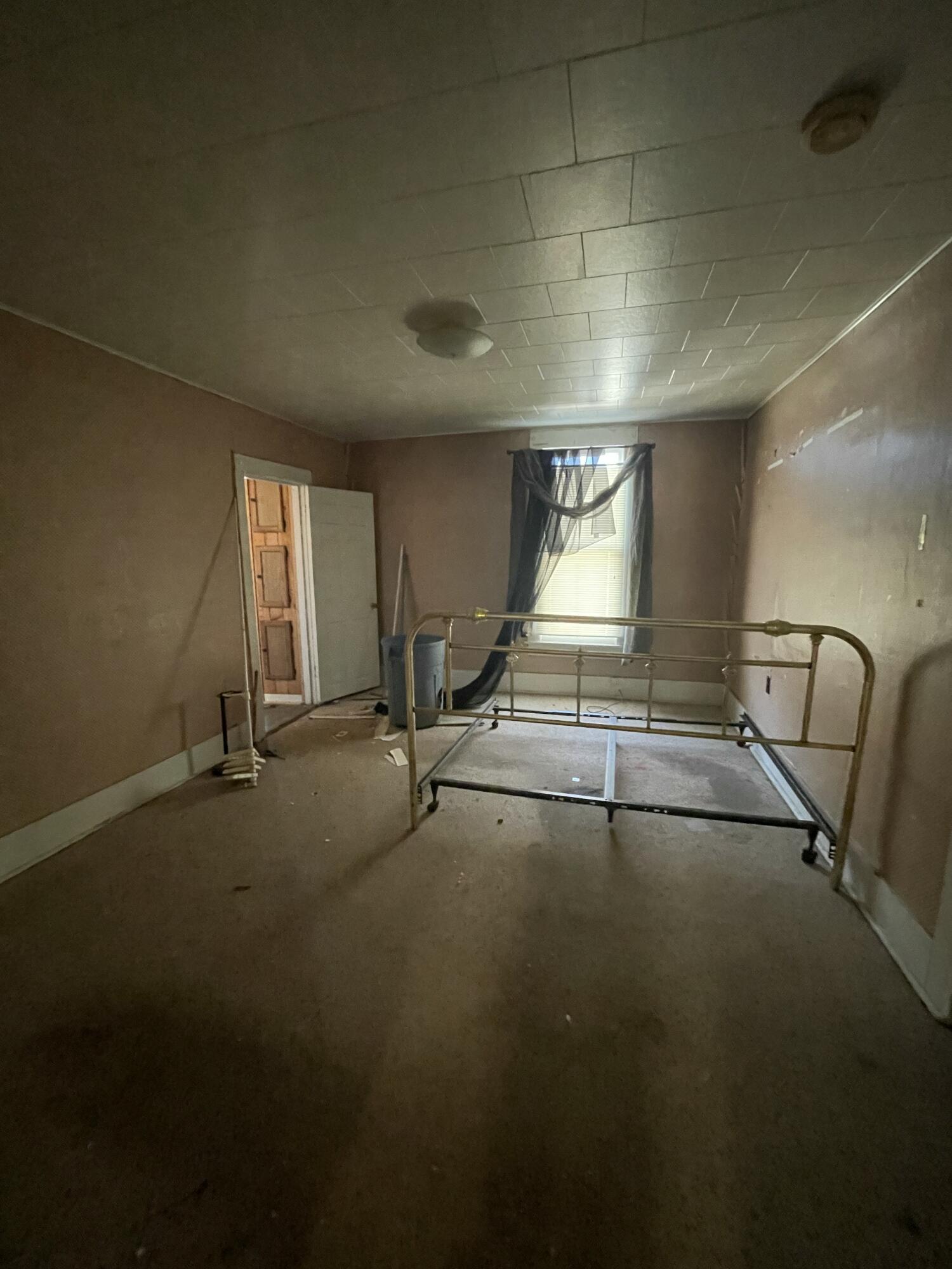 Bedroom with a metal bed frame, curtained window, and peeling patches on the wall.