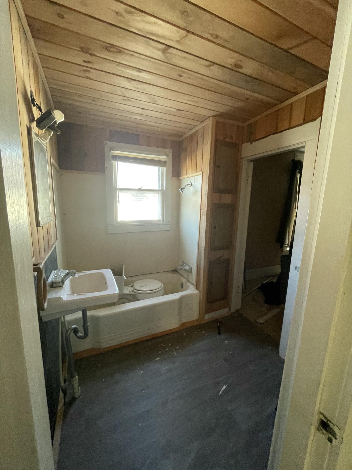 Bathroom with a bathtub, toilet, wall-mounted sink, and wood-paneled ceiling.
