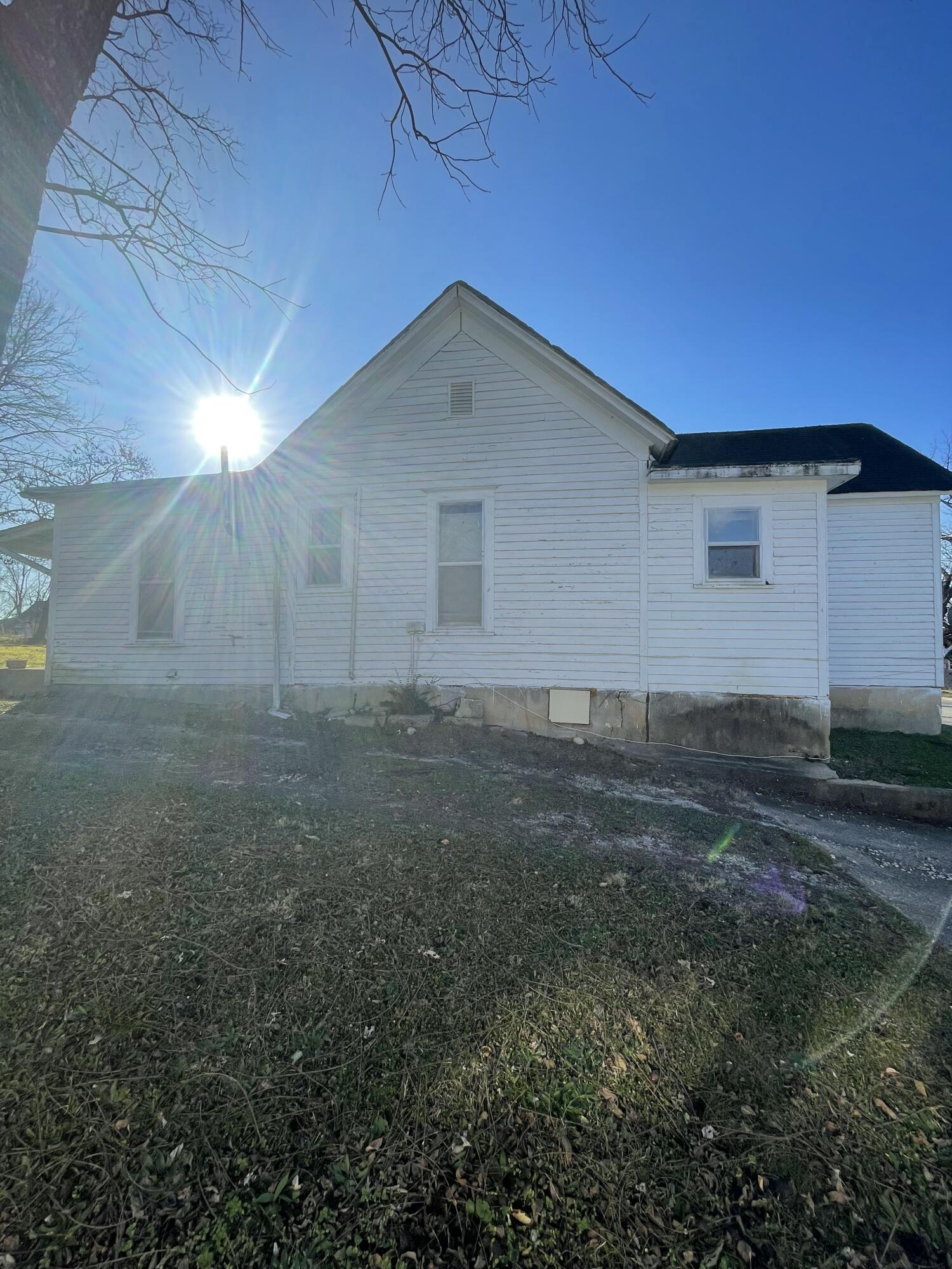 White-sided house with a prominent gable and dormant yard in bright winter sunlight.