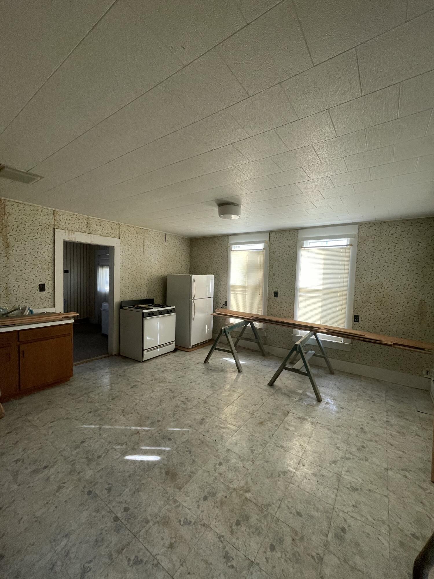 Mostly empty kitchen with a white stove, refrigerator, two blinded windows, and boards on sawhorses.