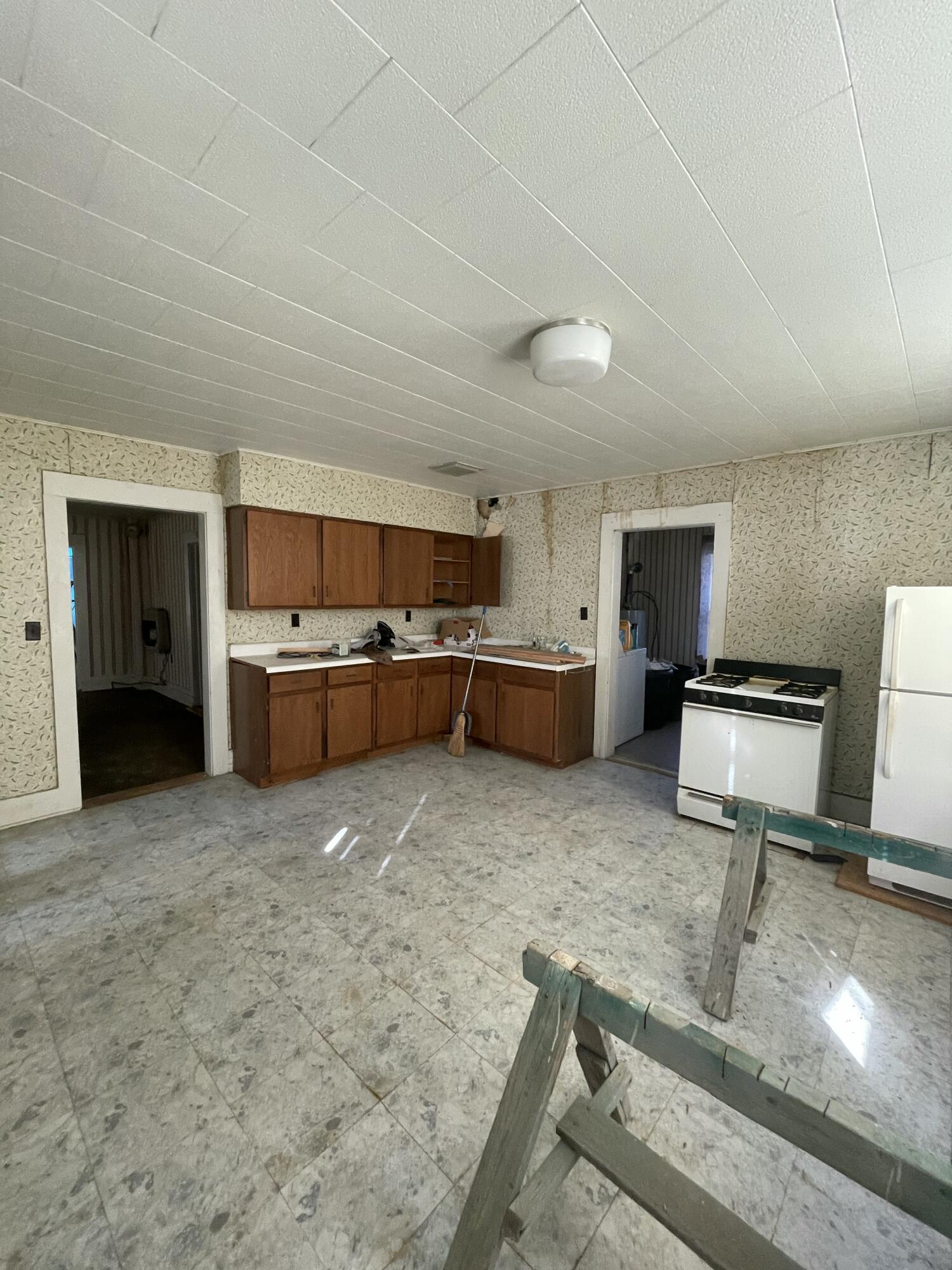 Vacant kitchen with wood cabinets, patterned wallpaper, and a sawhorse in the foreground.